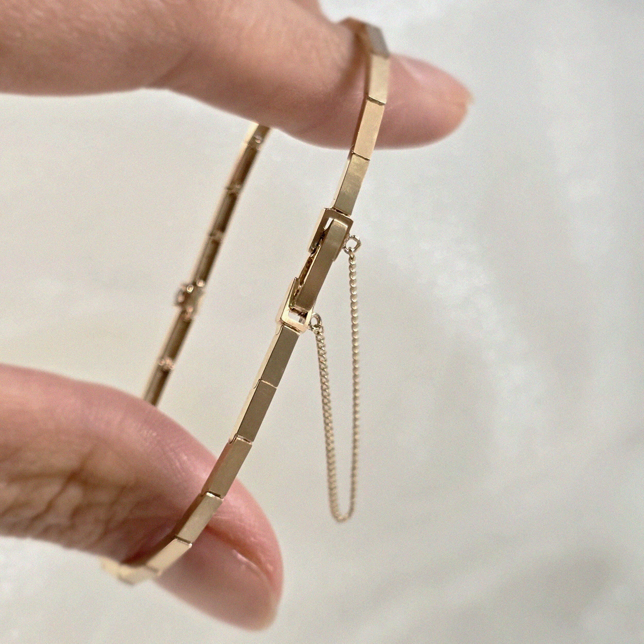 Close-up of the Grazia Diamond Bracelet held between fingers, showing the secure clasp and safety chain