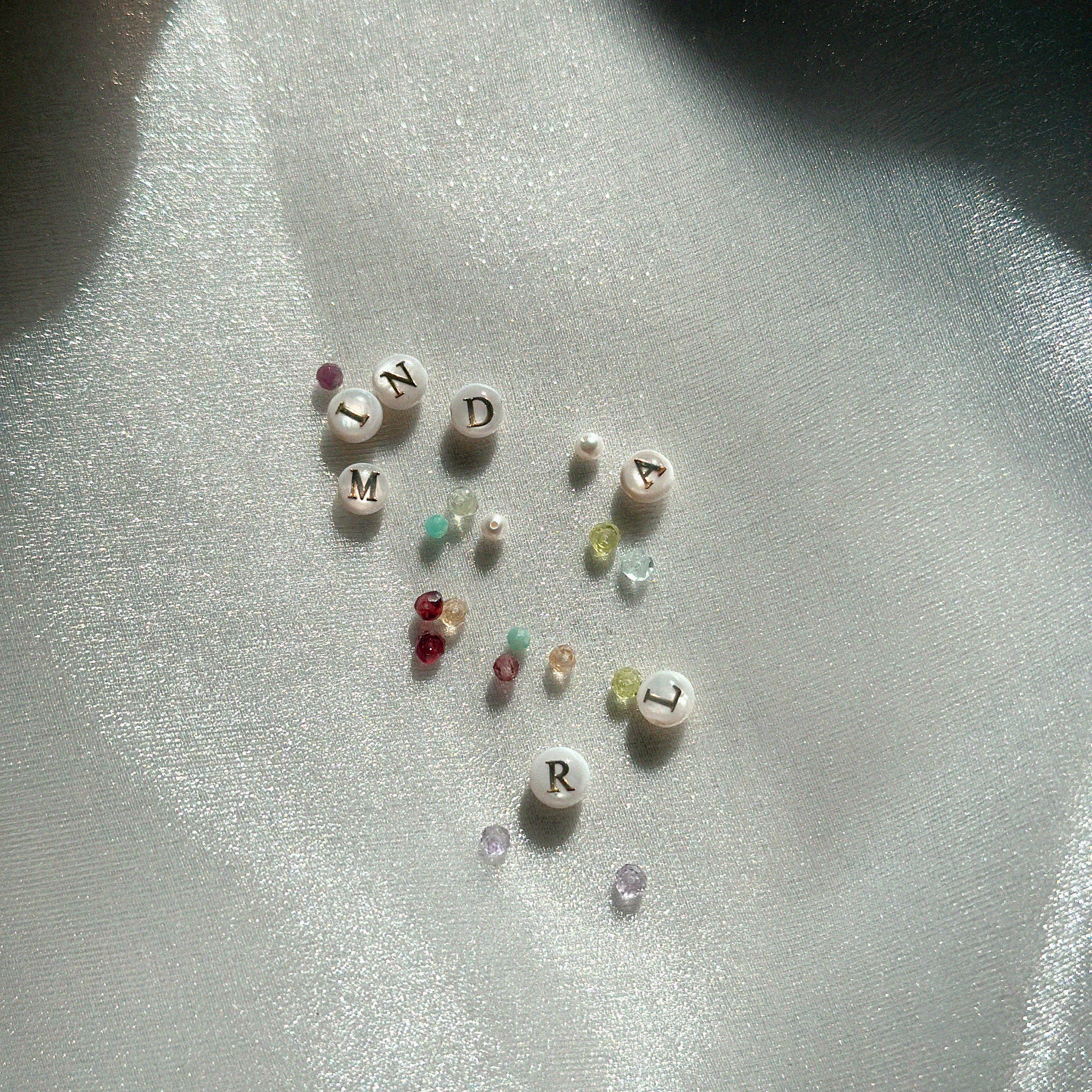 Small gemstones and mother of pearl initial charms on a reflective surface