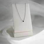Necklace with a black pendant on a white stand against a white background