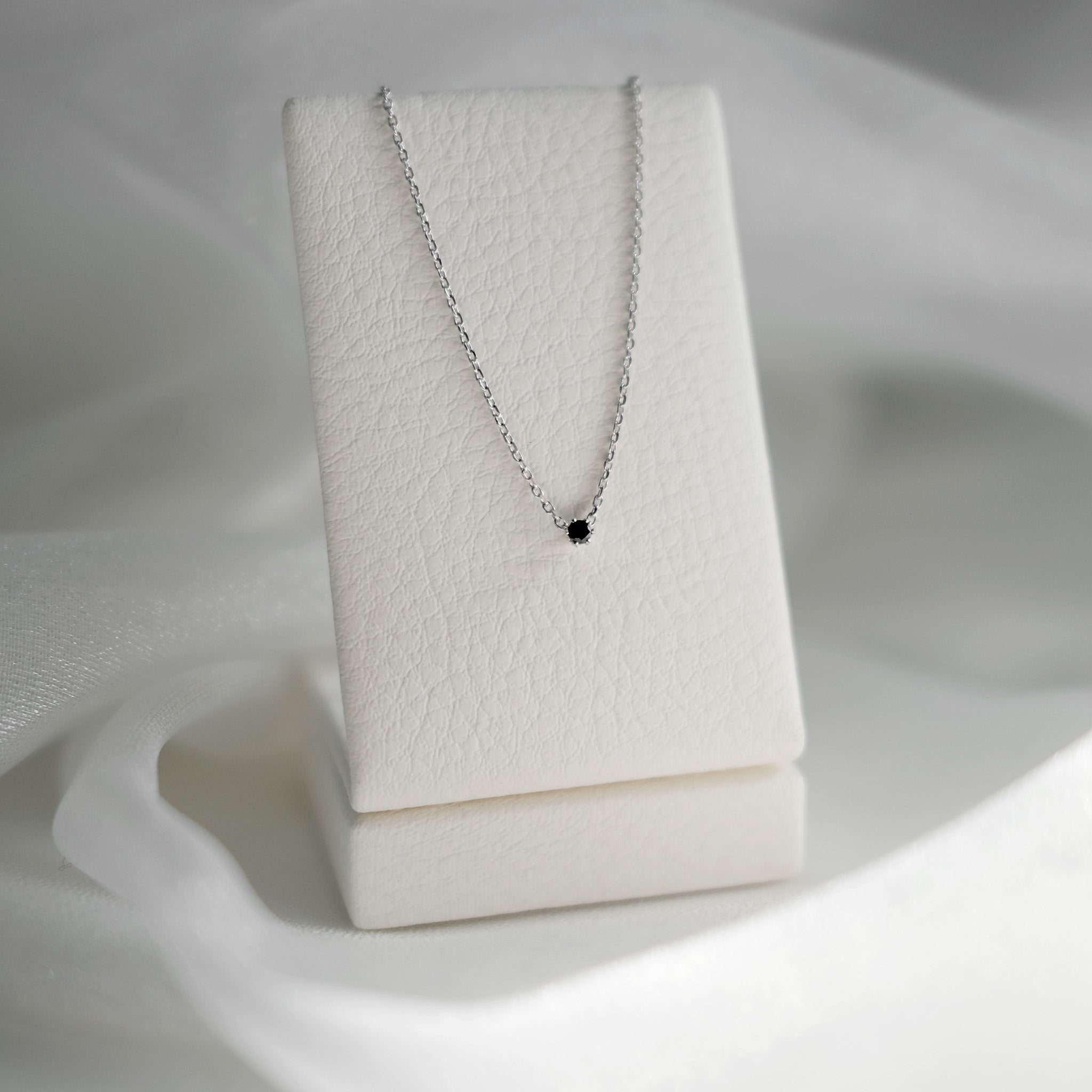 Necklace with a black pendant on a white stand against a white background