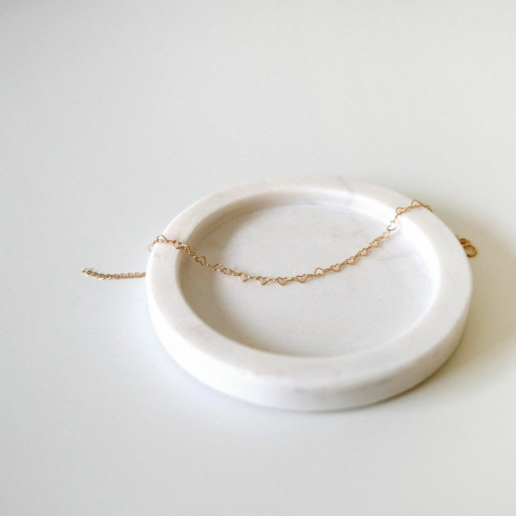 Linked heart bracelet draped naturally on soft neutral-toned jewelry tray