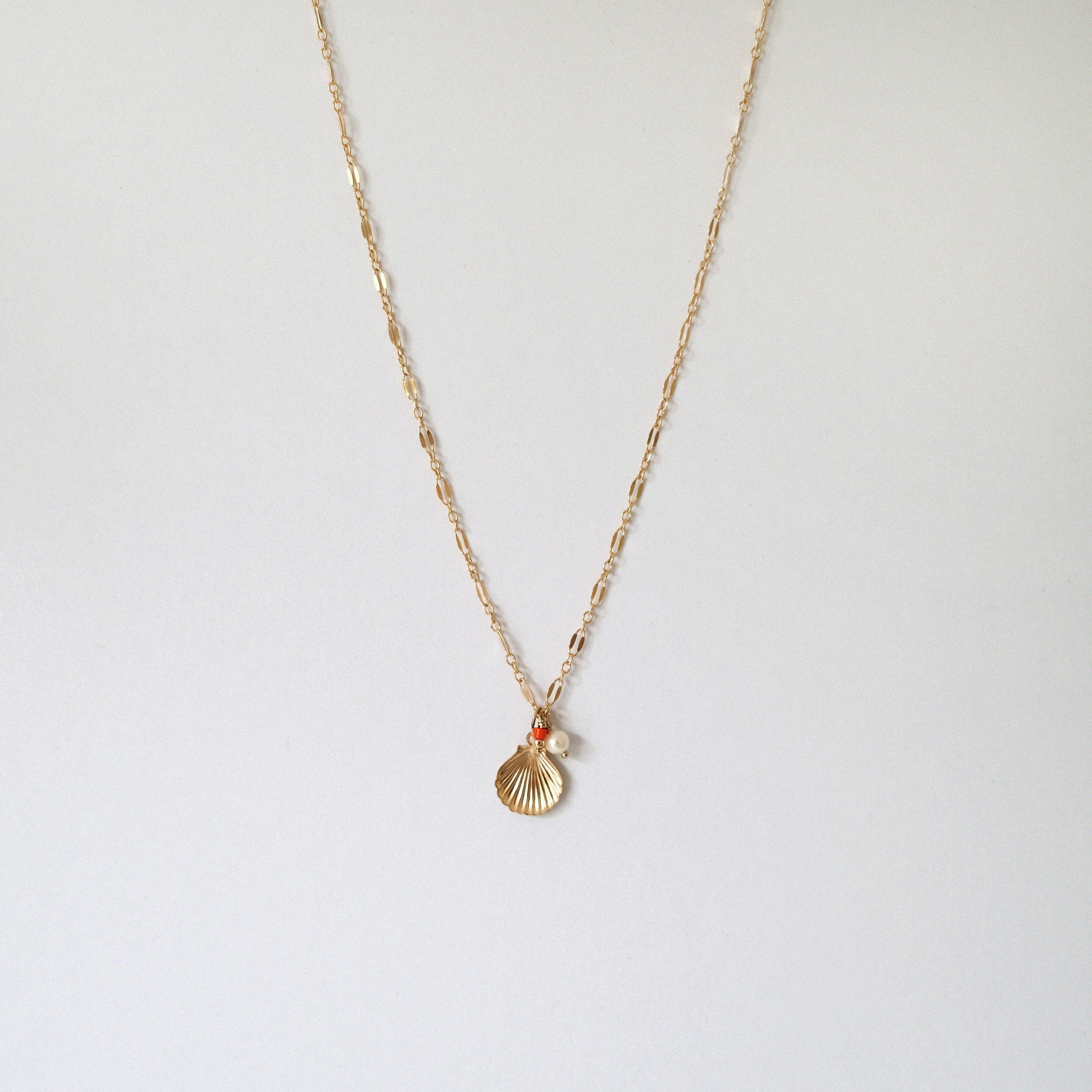 Gold filled necklace with shell pendant, pearl, and coral beads laid fla