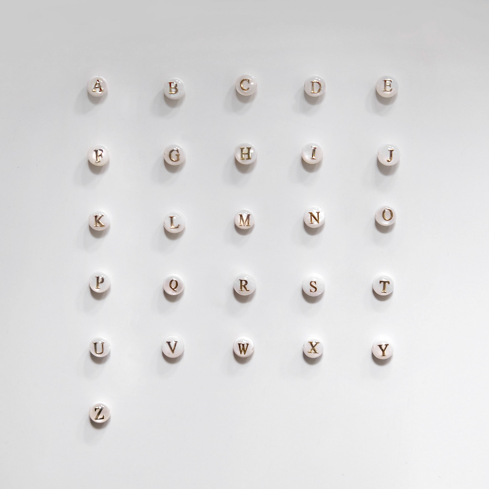 Mother of pearl initial charms spelling out 'ABCDEFGHIJKLMNOPQRSTUVWXYZ' on a light gray background