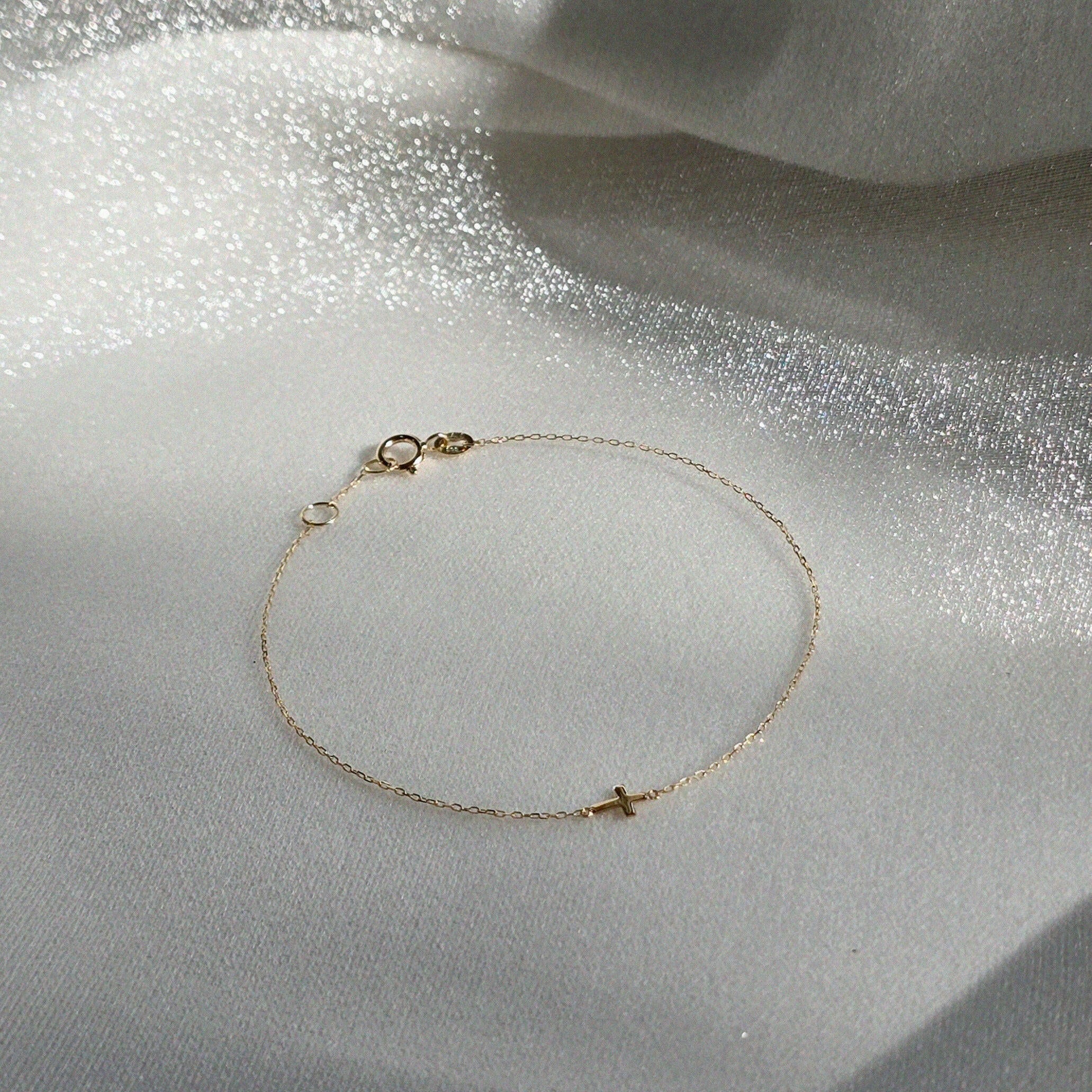 Petite Cross Bracelet displayed on shimmery textured fabric