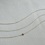 Three dainty 14K gold chain bracelets displayed on a soft textured fabric, including one with a small cross charm