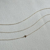 Minimalist gold bracelets with fine chain links laid flat on cream-colored textile background