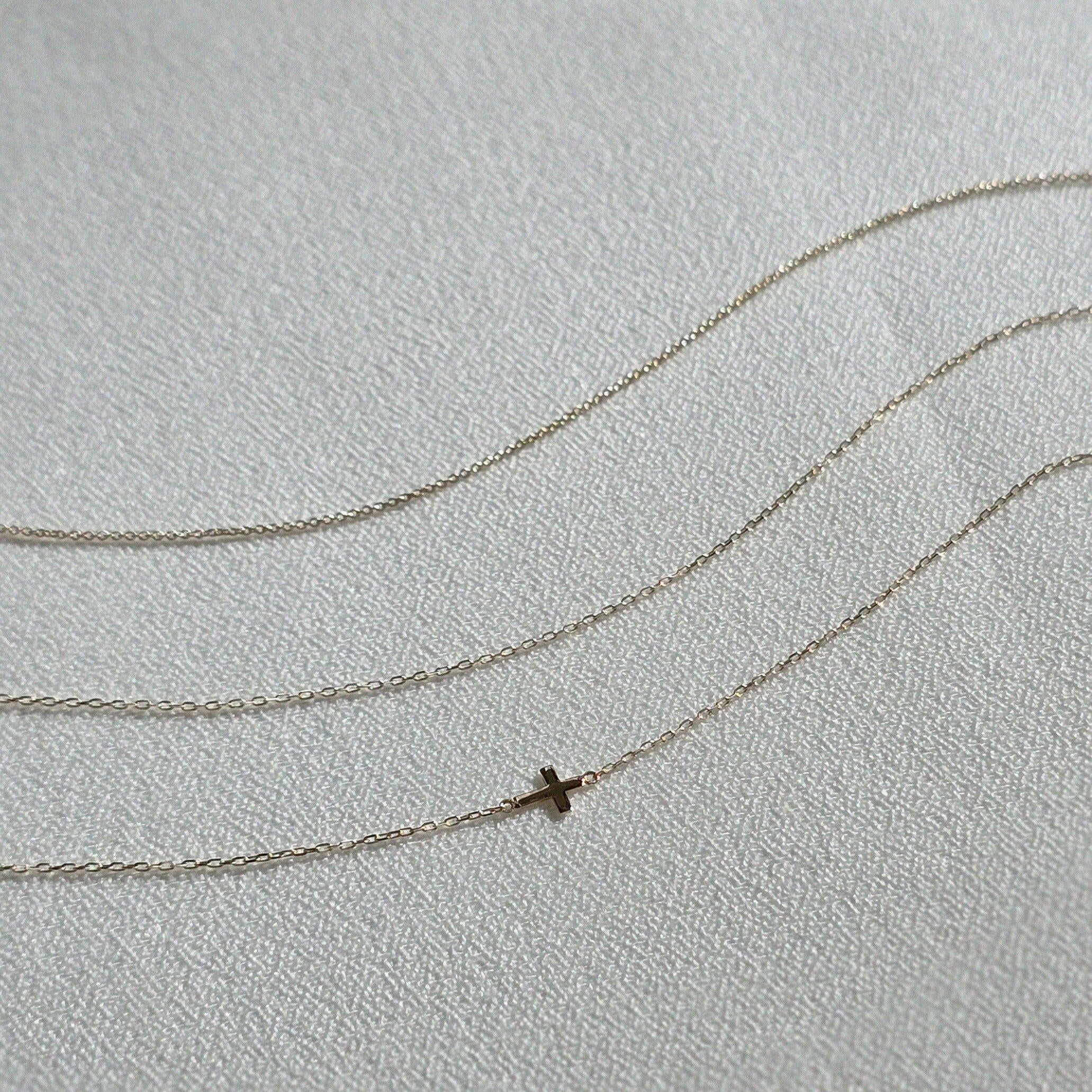 Minimalist gold bracelets with fine chain links laid flat on cream-colored textile background