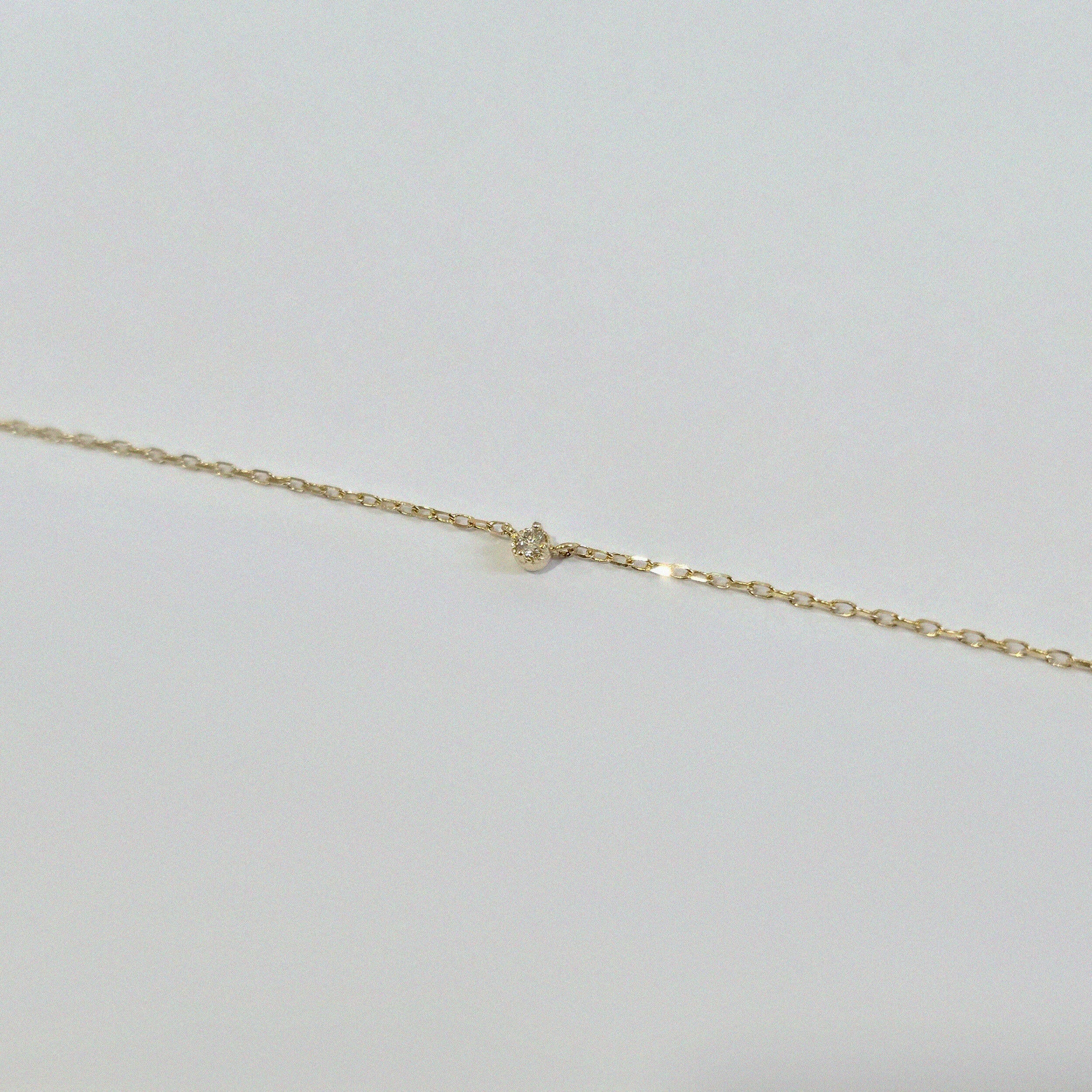 Detailed image of small brilliant diamond on a minimalist gold chain with polished finish