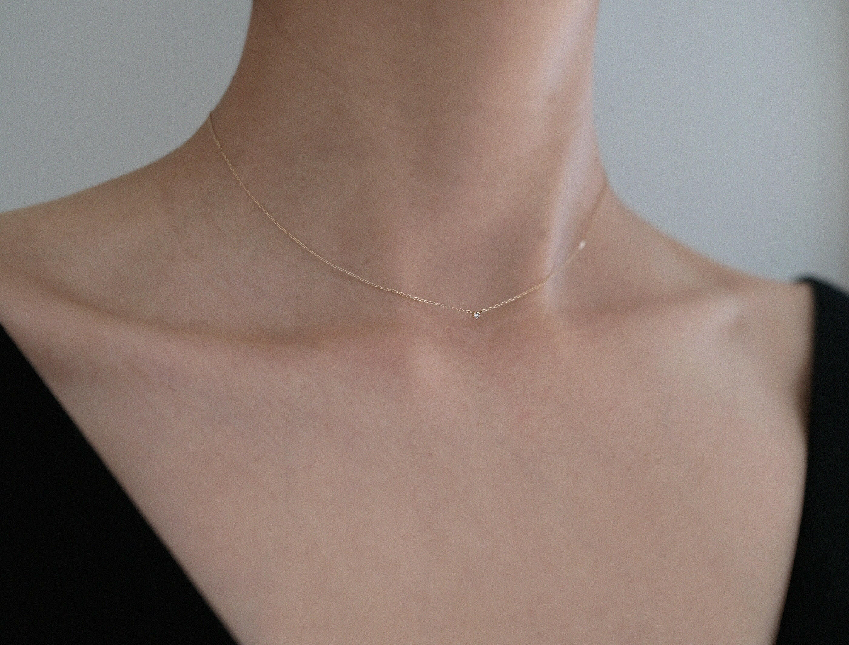 Model wearing petite diamond necklace with black V neck top, close-up chest shot