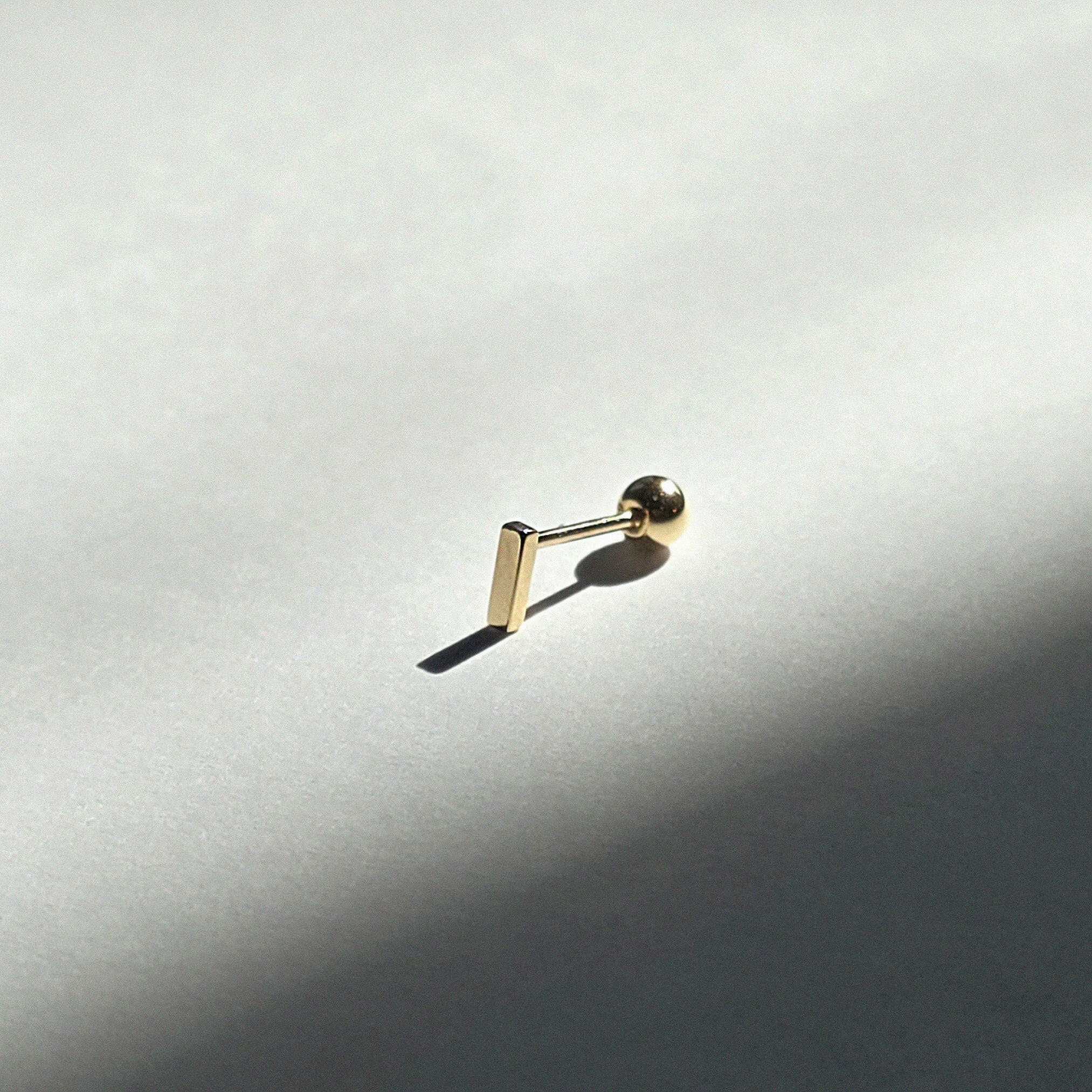 Polished solid gold bar stud shown on white background from side view
