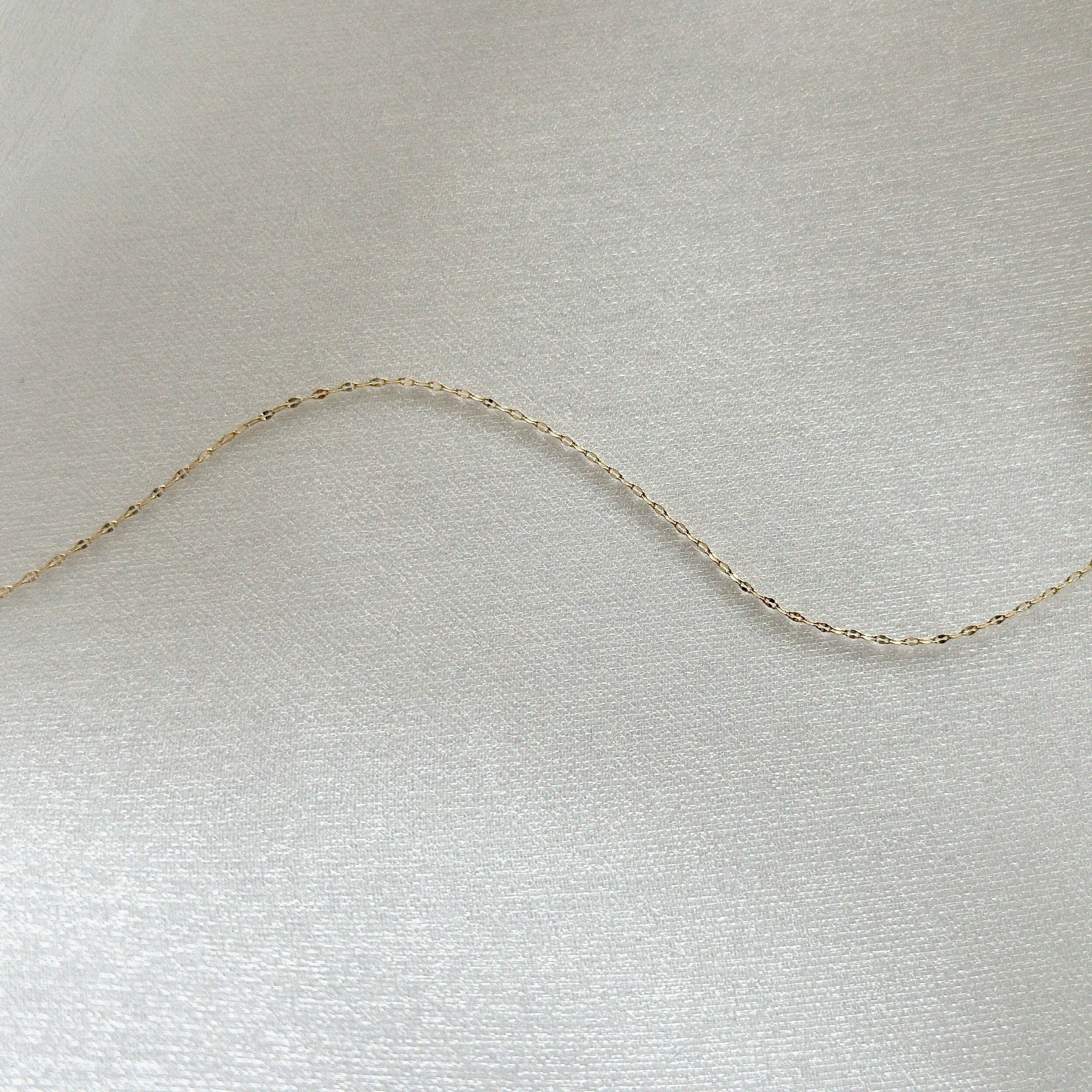 Close-up of the 14K Roma Chain Bracelet’s fine gold links displayed on soft satin fabric