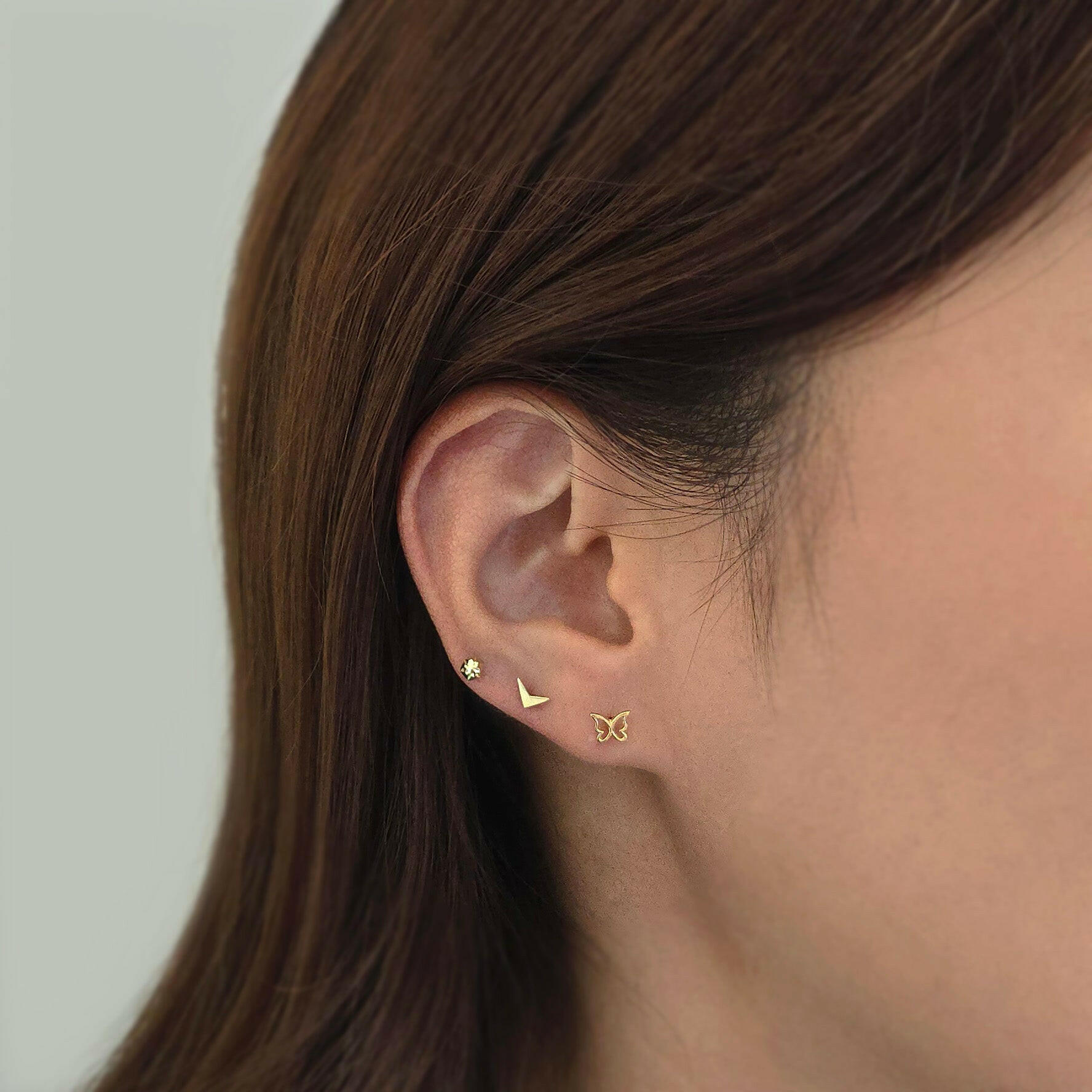 Geometric gold earring stacked with minimalist studs in curated ear setup