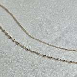 14K Capri Chain Bracelet and 14K gold bracelet with square details displayed on soft fabric