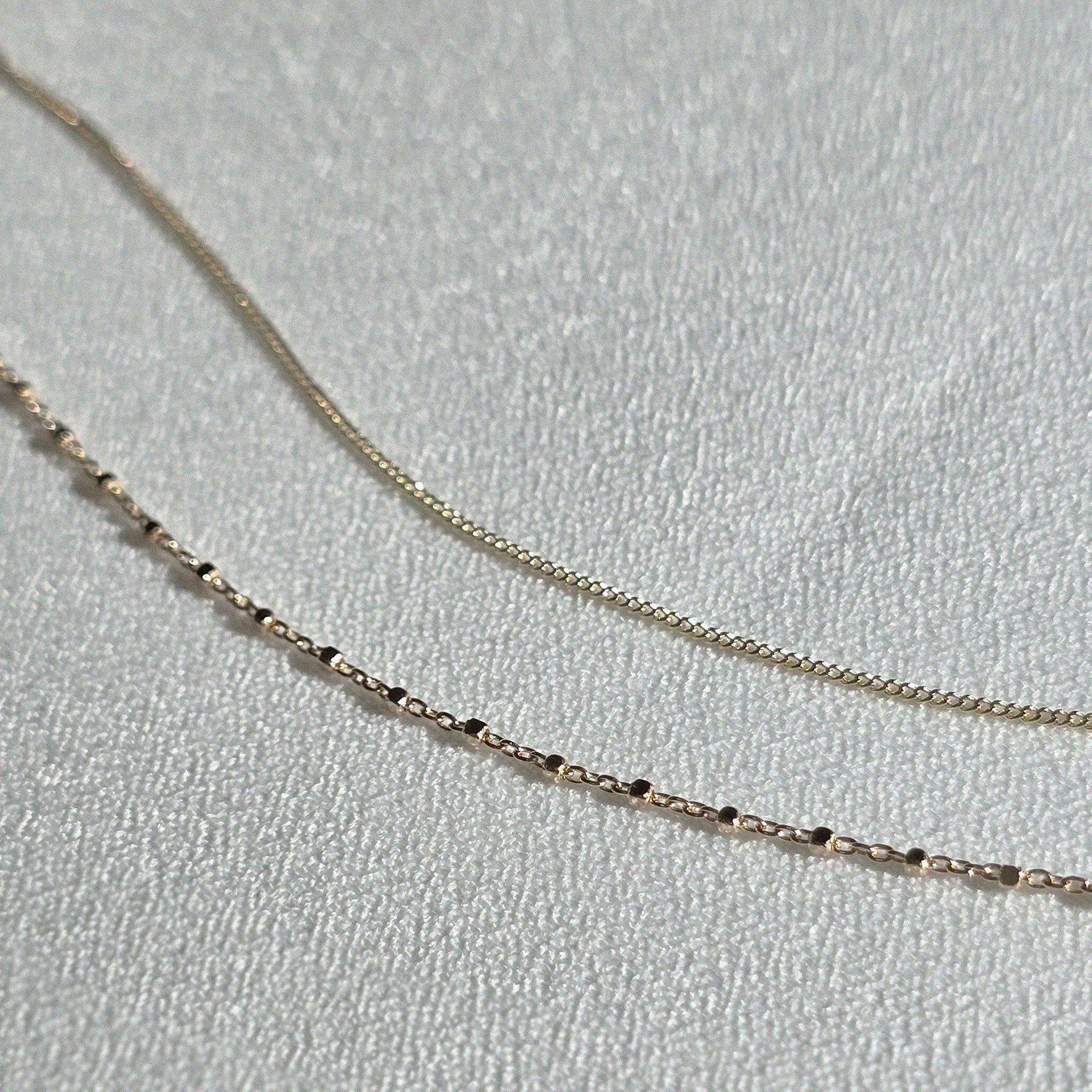 14K Capri Chain Bracelet and 14K gold bracelet with square details displayed on soft fabric