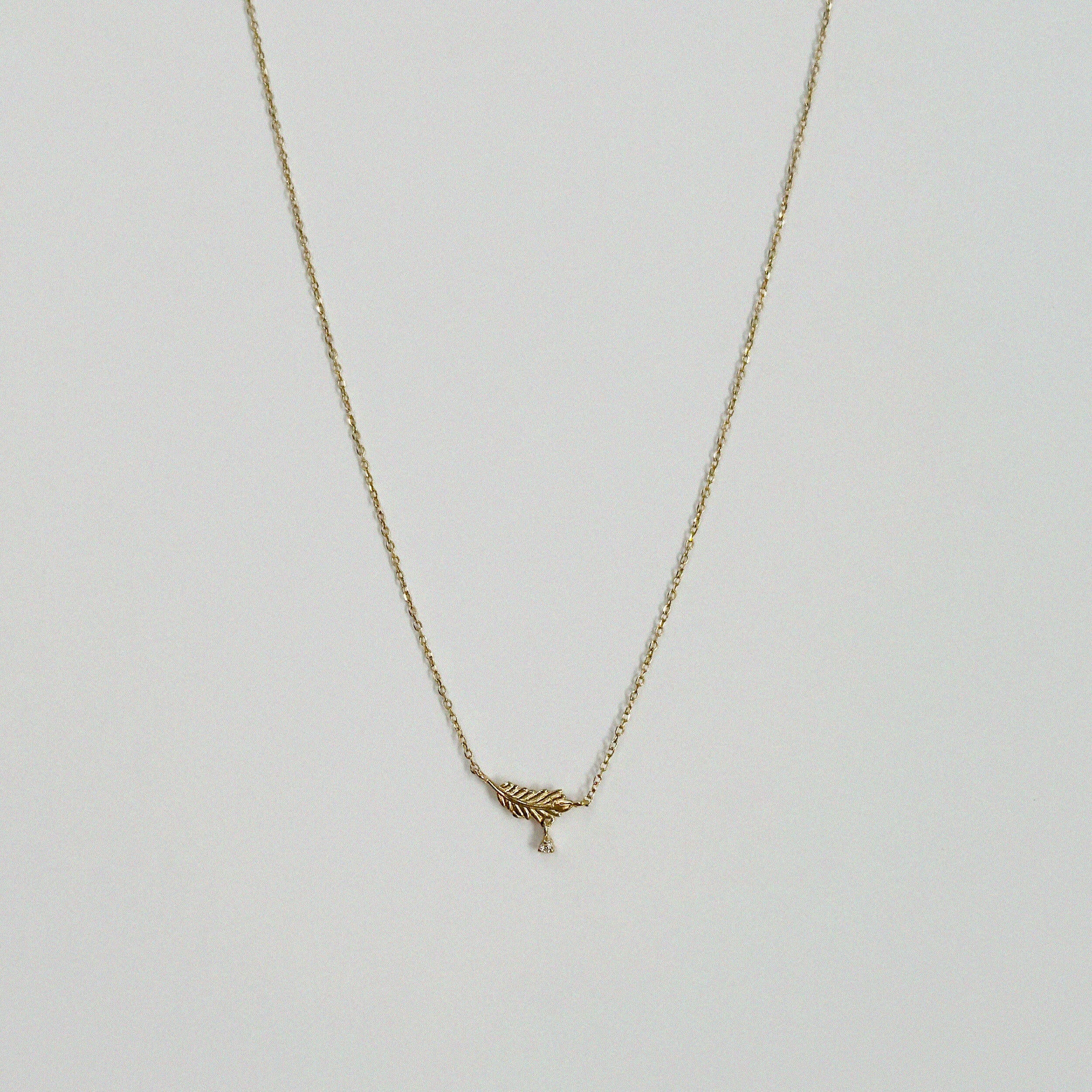 Full front view of 14K Leaf With Crystal Necklace laid flat on neutral surface