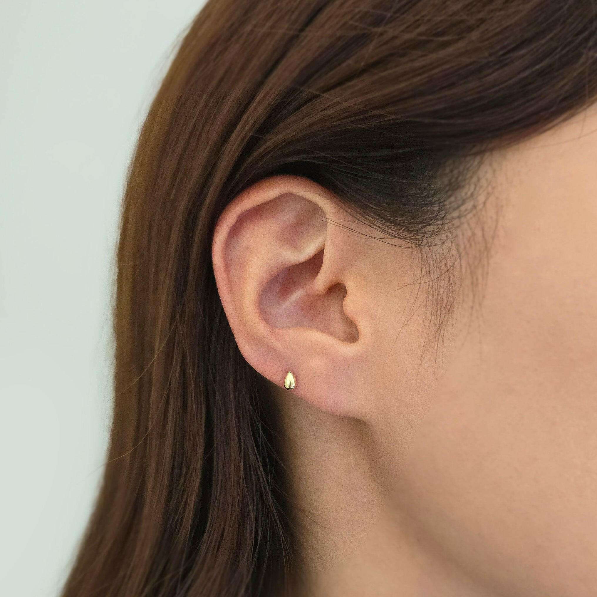 14K gold teardrop cartilage earring worn on low helix for understated elegance