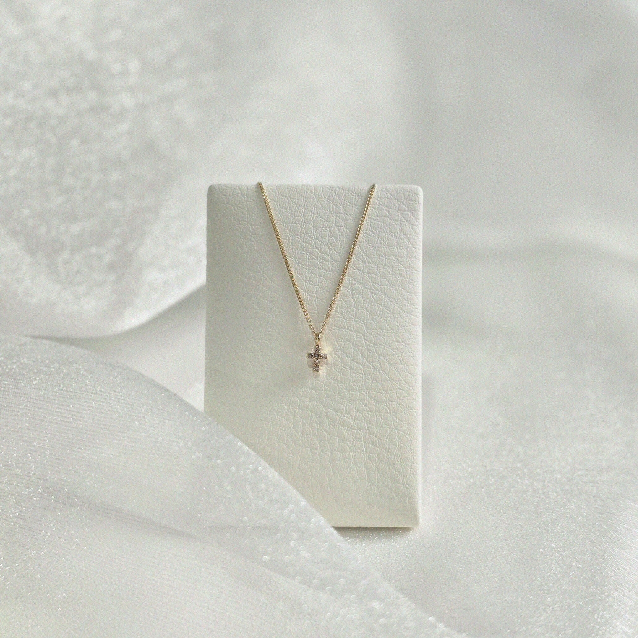 Diamond cross necklace displayed on soft leather necklace stand – balanced drape and elegant glow