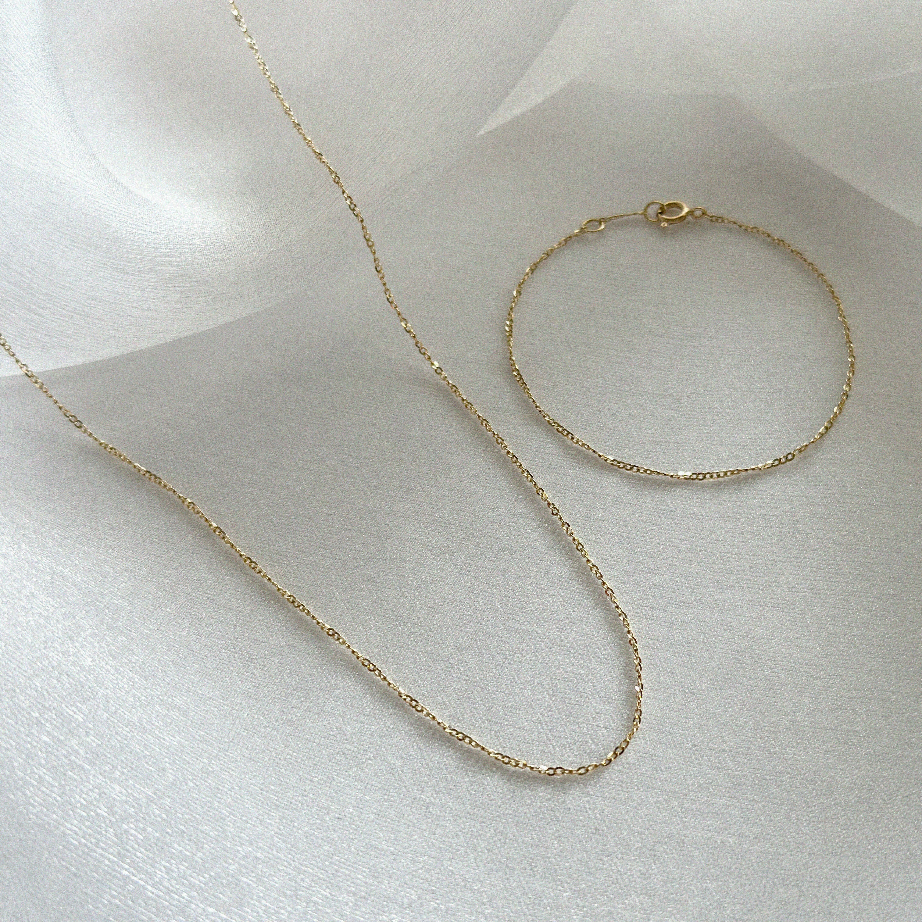 Twisted gold chain bracelet and necklace set laid out elegantly on cream-toned textile background