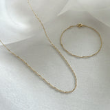 Torino Chain Necklace and matching bracelet displayed flat on a soft neutral background, showcasing their twisted 14K gold design with delicate light reflections.