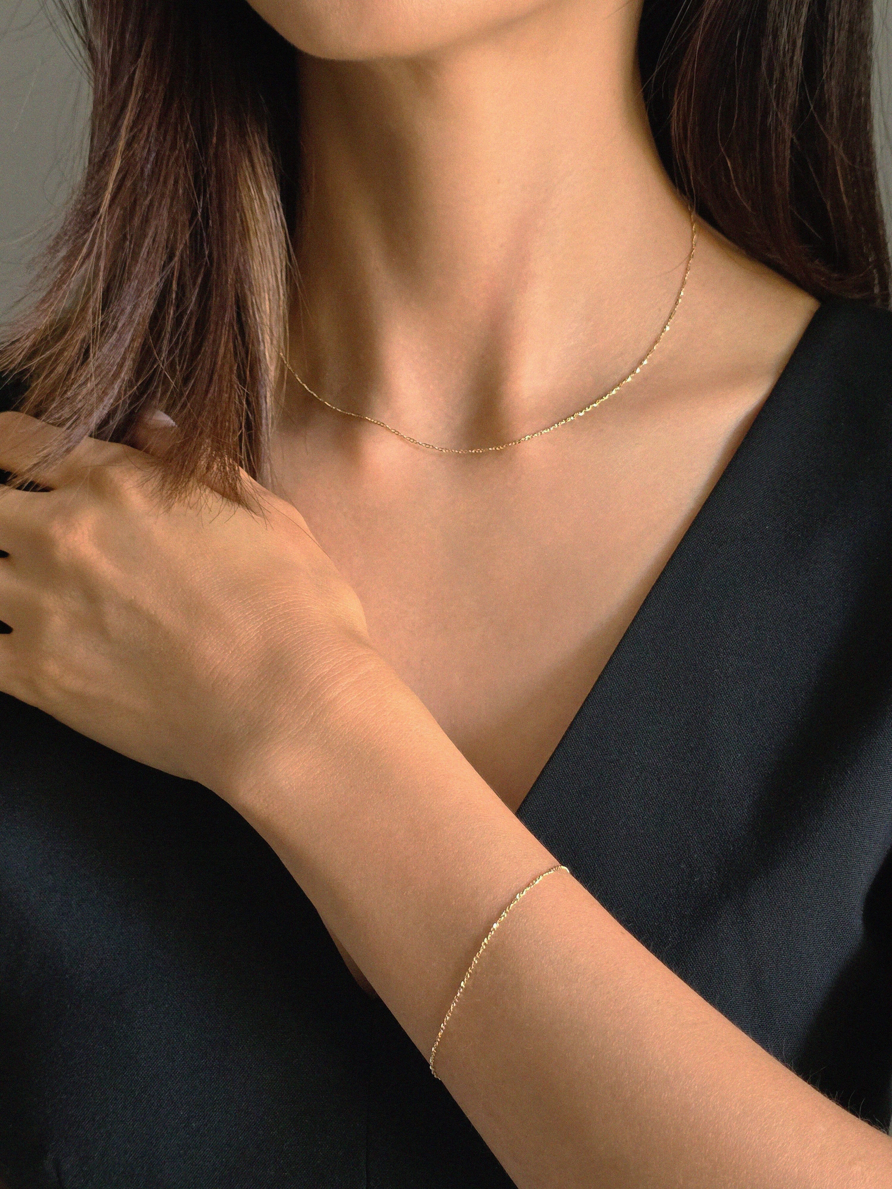 Model wearing matching 14K gold twisted chain necklace and bracelet, styled with a black V-neck top