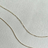 Dainty box chain and rectangular link bracelet arranged in flowing curves on a textured surface