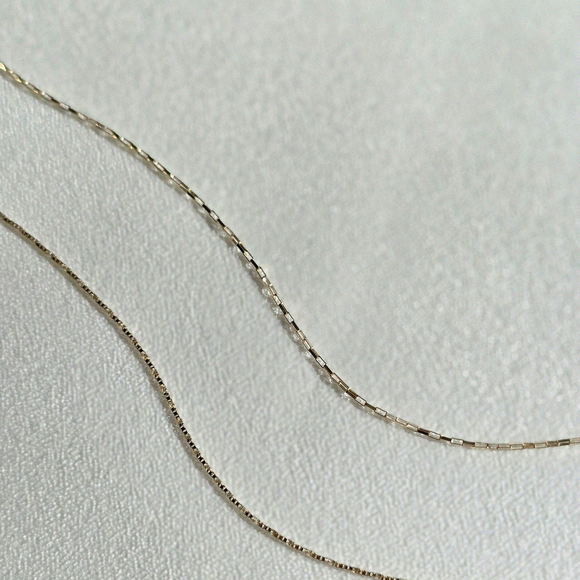 Dainty box chain and rectangular link bracelet arranged in flowing curves on a textured surface