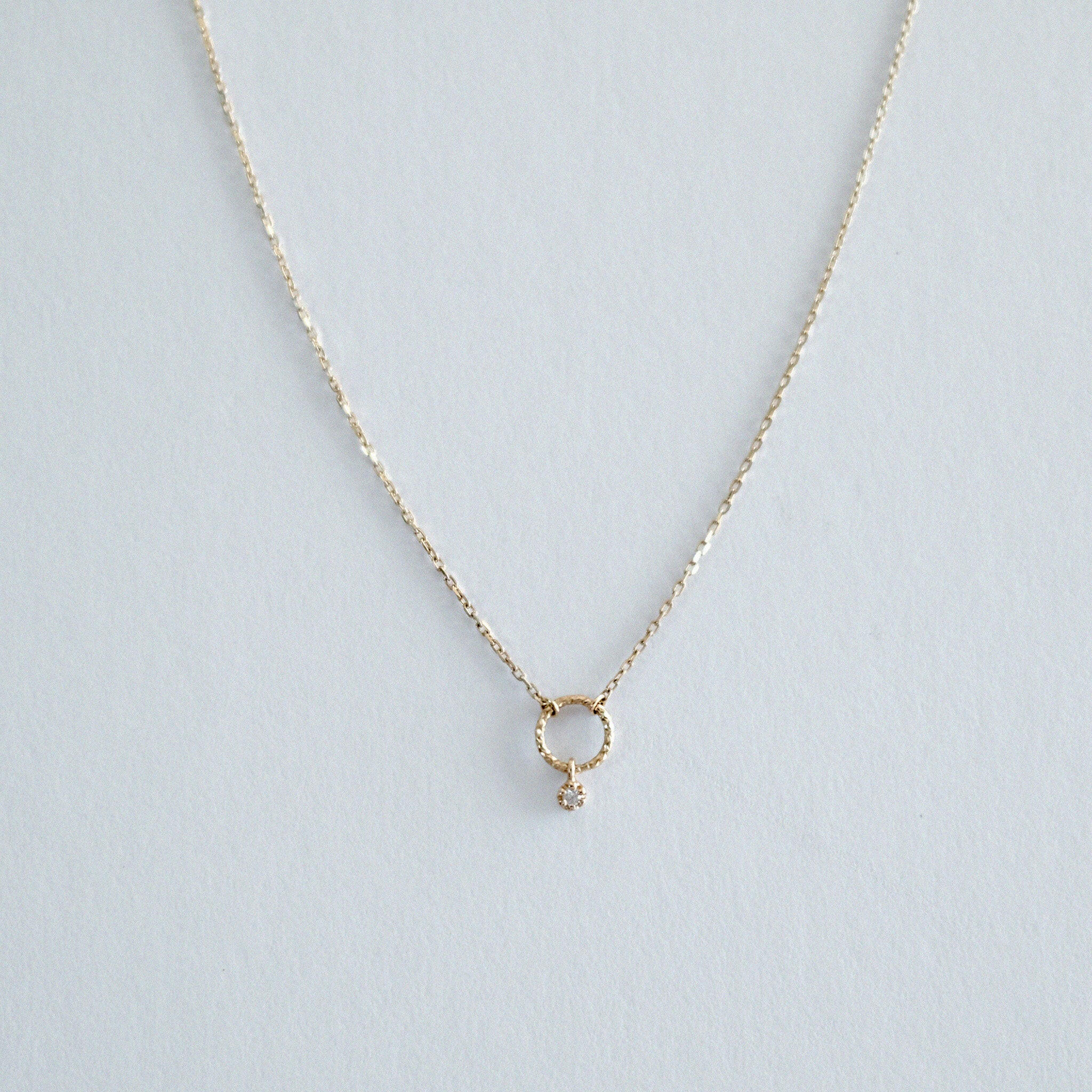 Overhead close-up showing the hammered texture of the 14K gold circle pendant and inset diamond