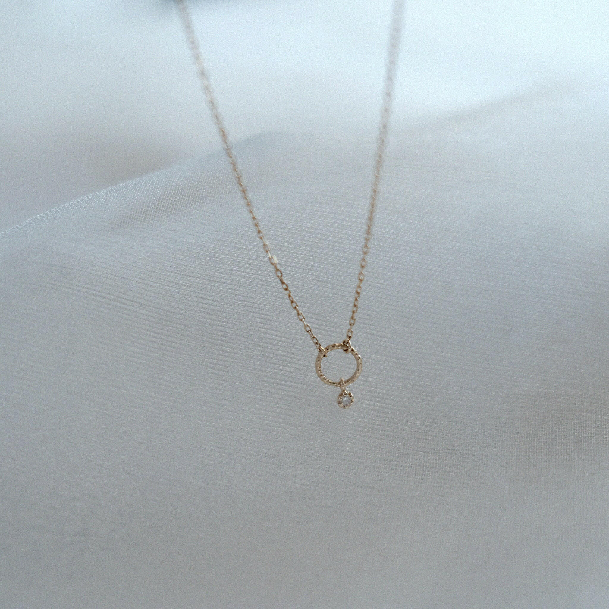 Minimalist display of the Circle with Diamond Necklace highlighting the textured gold and sparkling diamond
