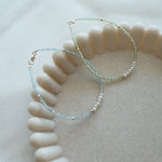 14K Gemma Beads Bracelet in Blue Apatite and Peridot variations displayed on a beige stone tray