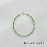 14K gold bracelet with green diopside stones laid flat on white background
