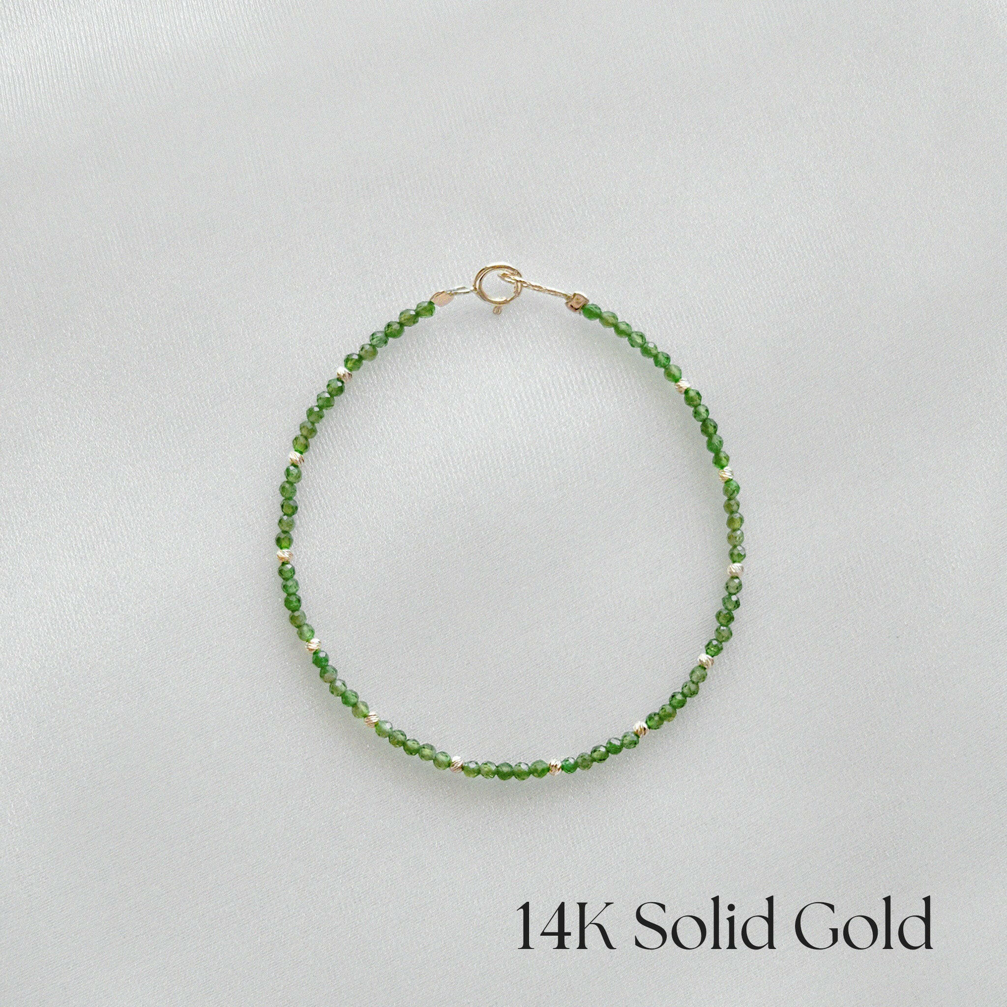 14K gold bracelet with green diopside stones laid flat on white background
