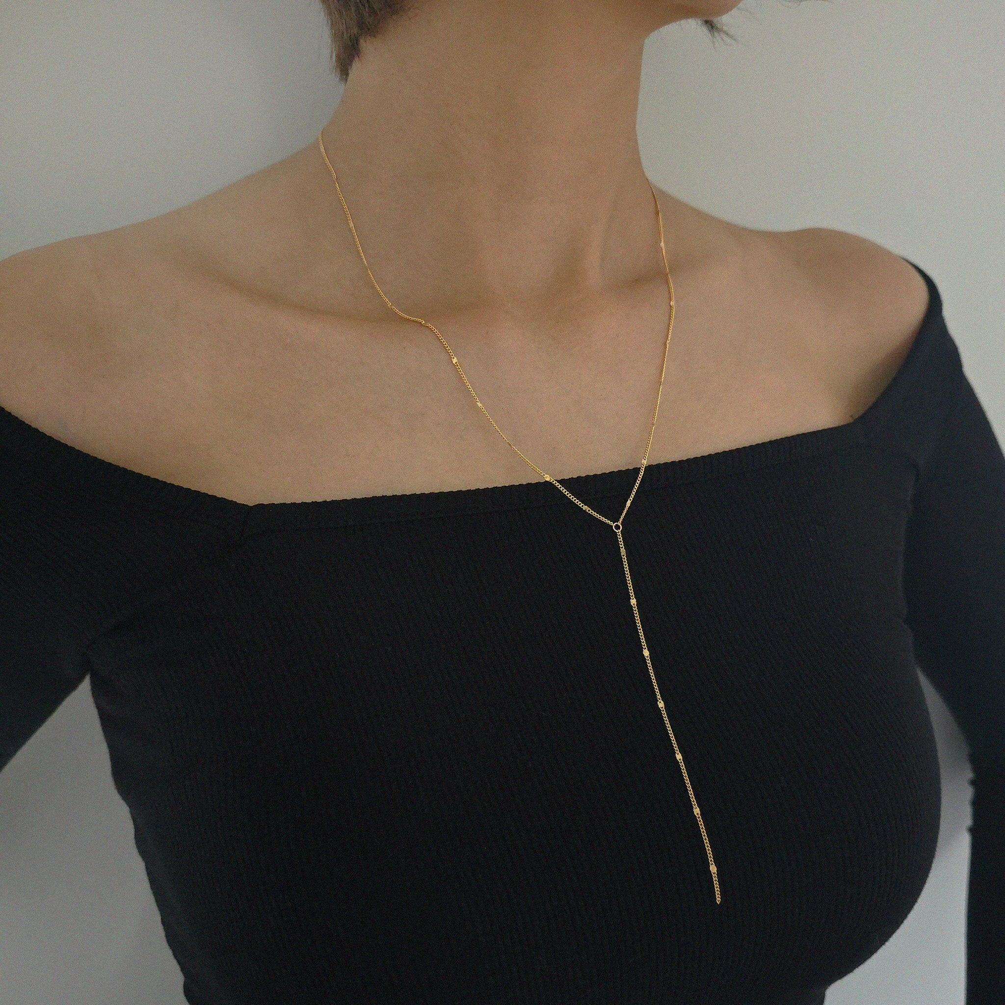 Gold necklace worn by a person in a black off-shoulder top against a neutral background