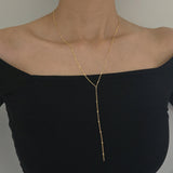 Gold necklace on a black top against a neutral background