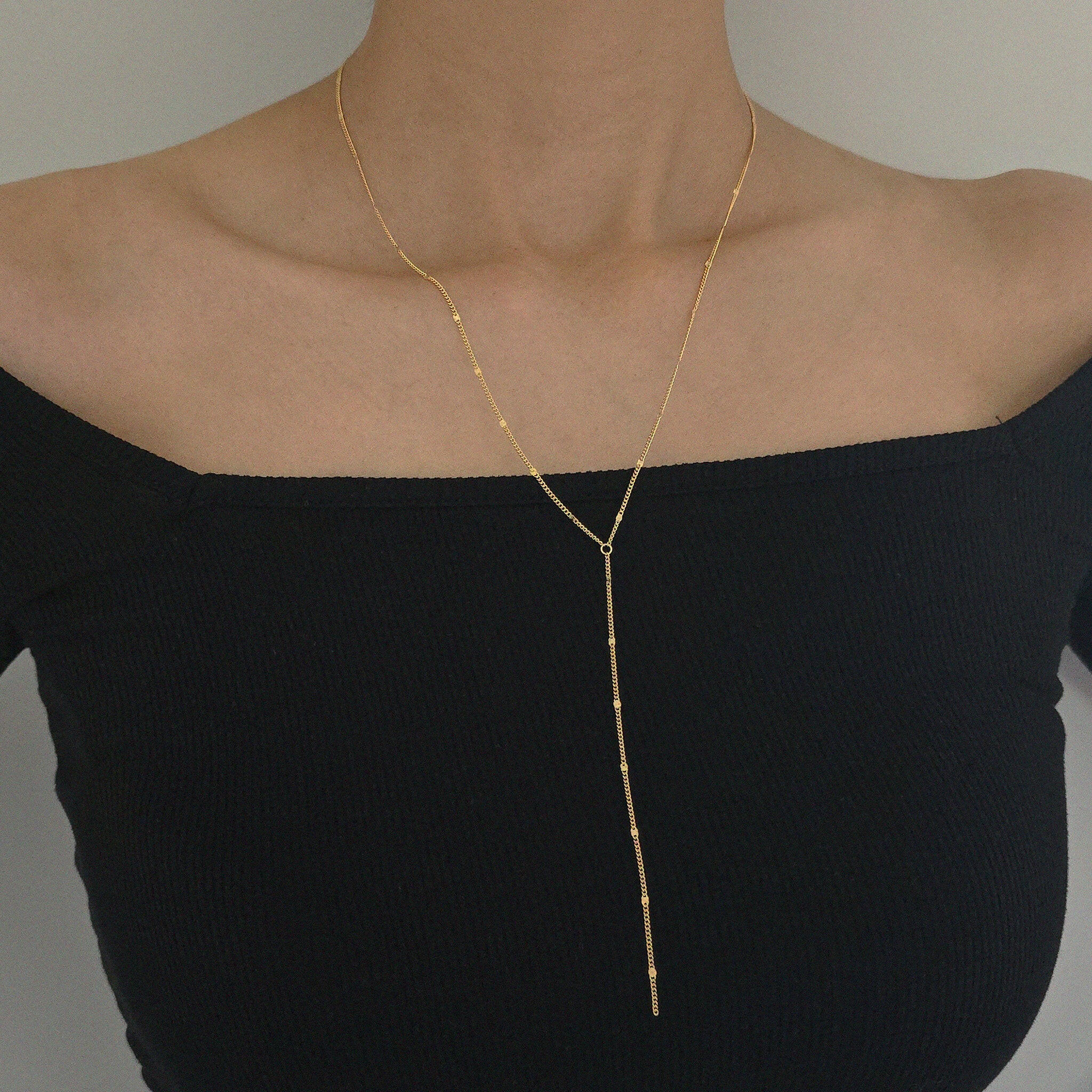Gold necklace on a black top against a neutral background