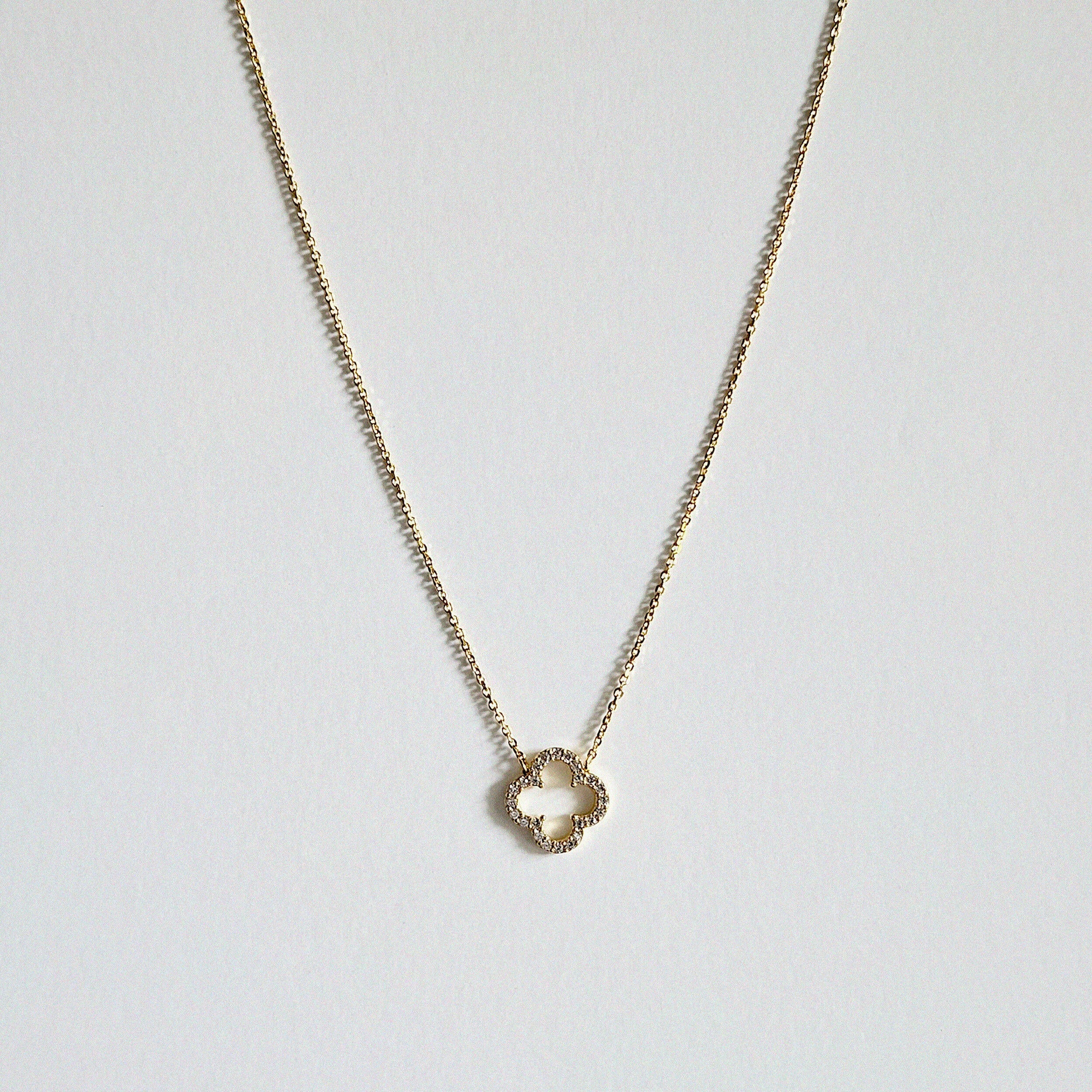 Crystal clover gold necklace with sparkling pendant laid flat in a soft curve