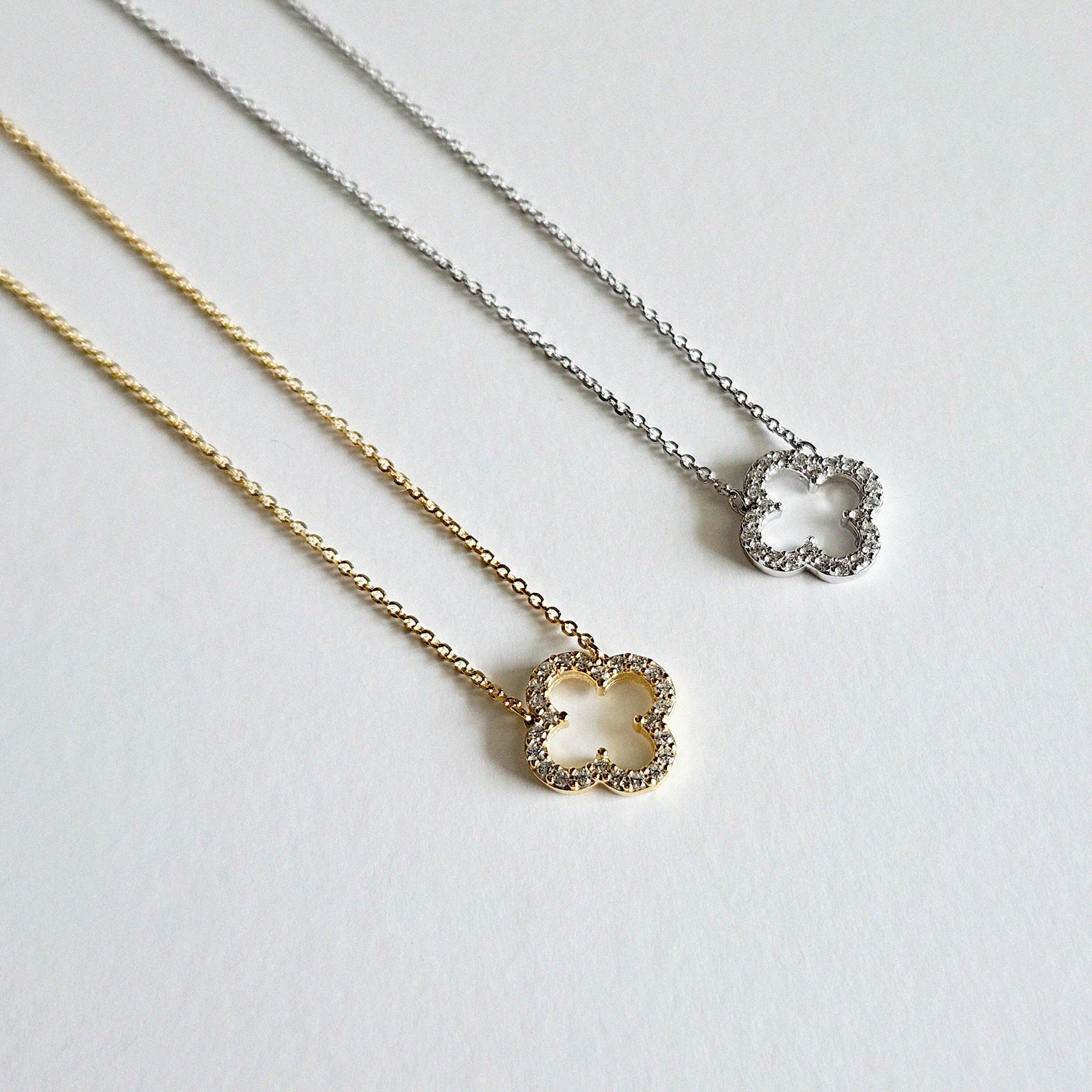 Gold and silver clover necklaces displayed side by side with cubic zirconia accents