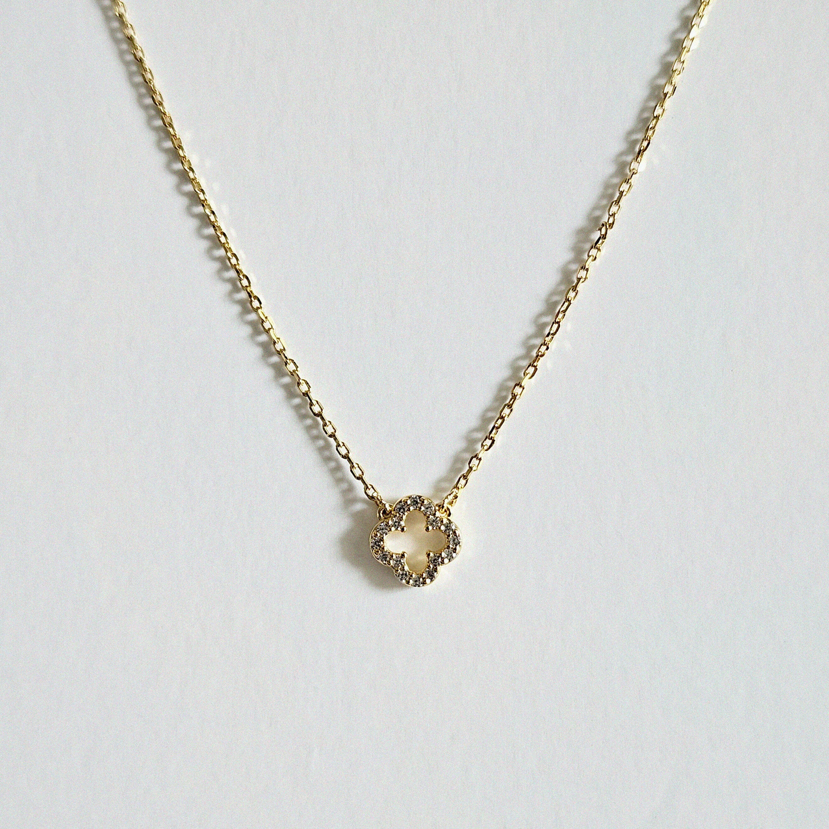 Petite 6mm gold clover pendant necklace with cubic zirconia laid flat on a light background