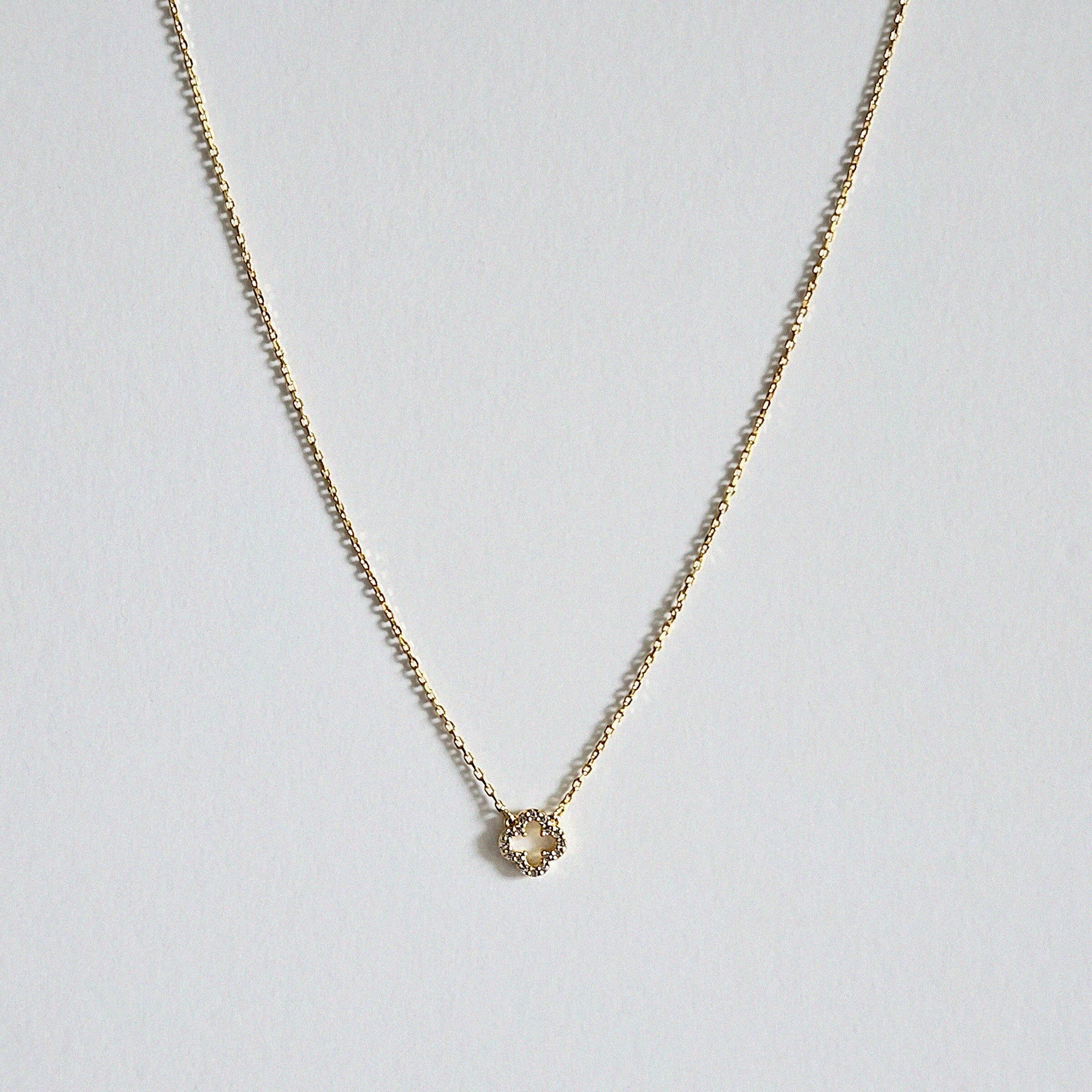 Petite 6mm gold clover pendant with dainty chain necklace laid flat on a light background