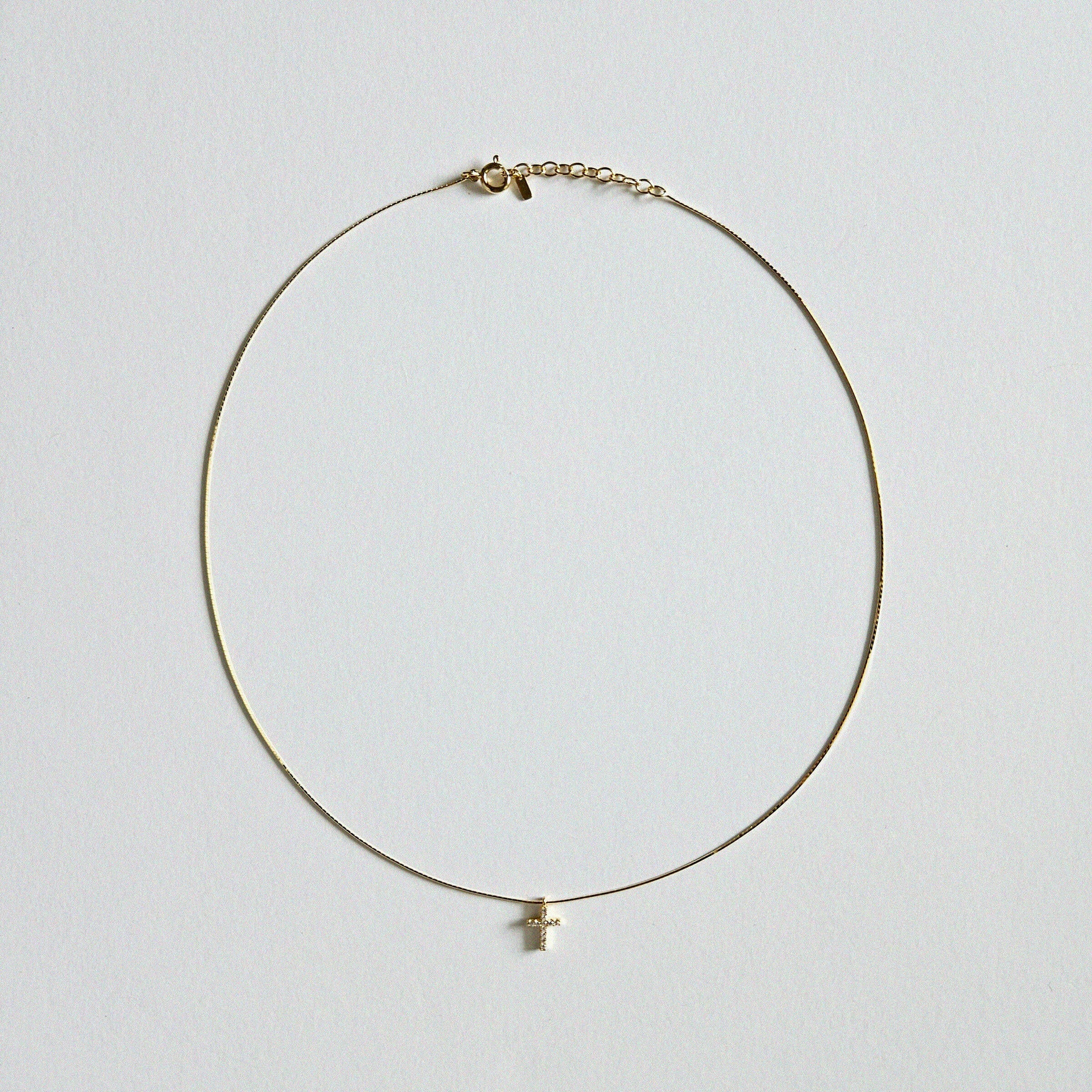 Dainty crystal cross necklace in gold laid flat on soft background with sleek snake chain
