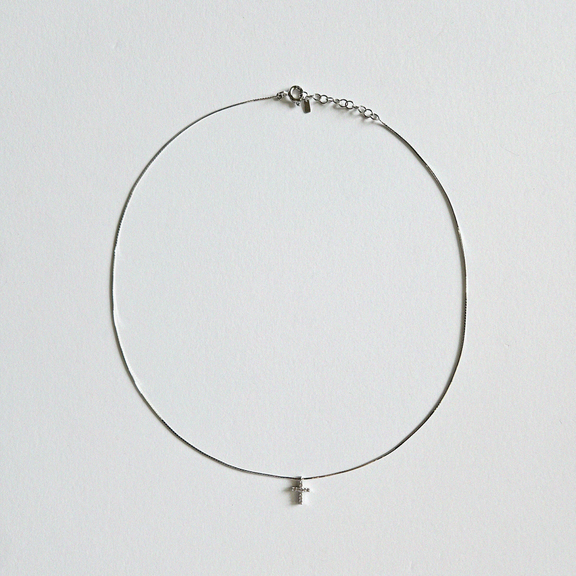 Dainty crystal cross necklace in silver laid flat on soft background with sleek snake chain