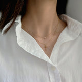 Profile of model showing bold cross pendant layered with 2mm petite cubic zirconia pendant necklace