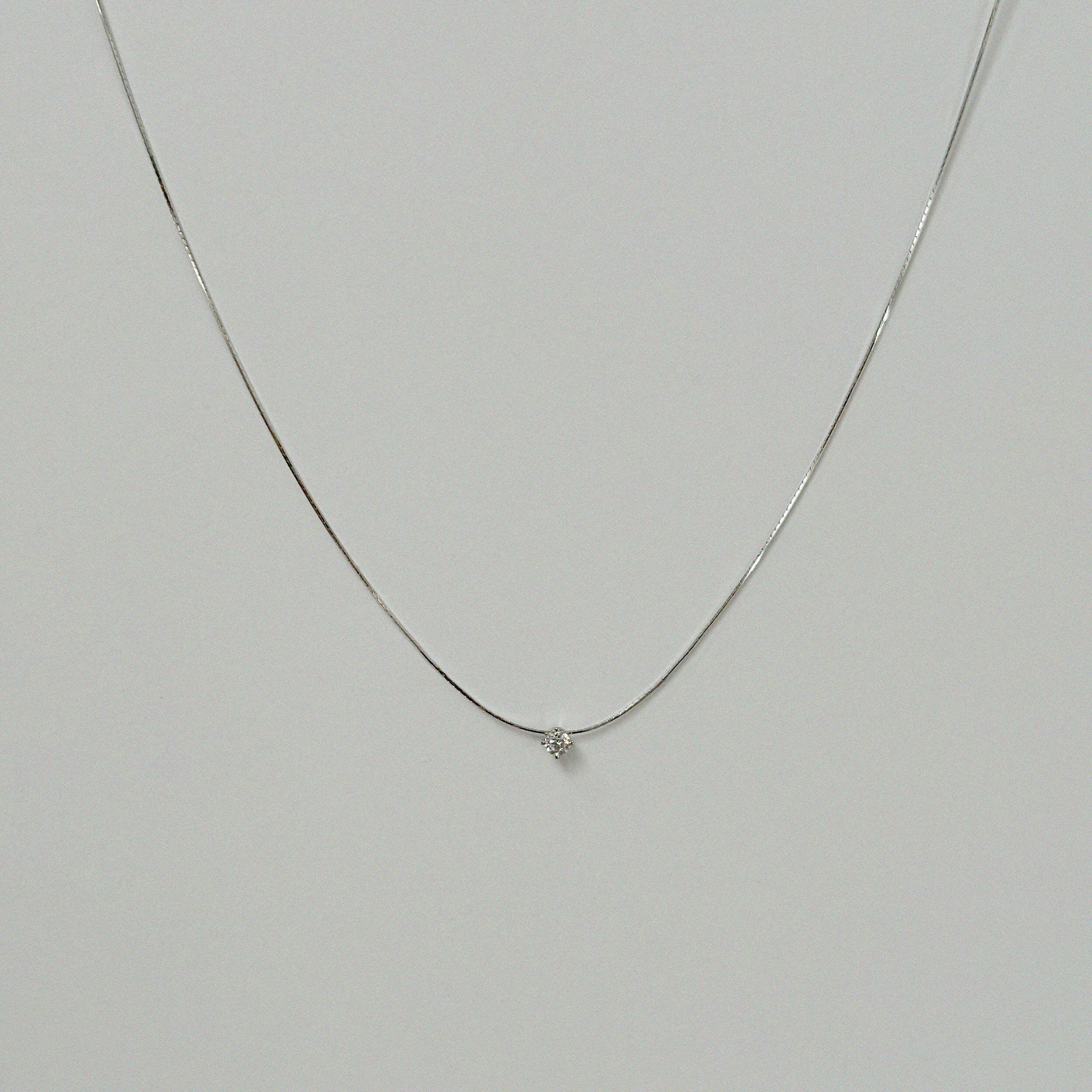 Petite crystal snake chain necklace in silver laid flat in a delicate curve with cubic zirconia accent.