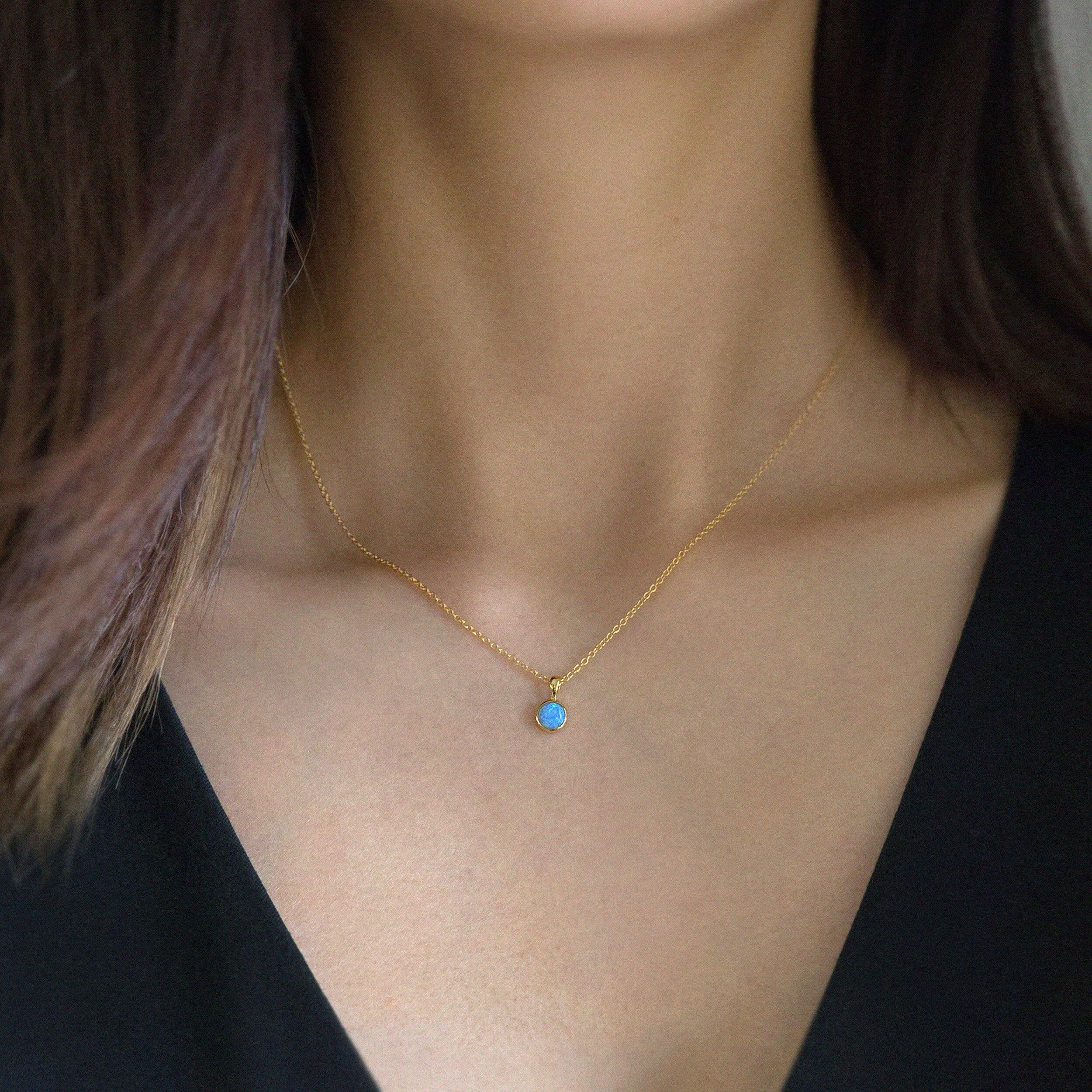 Model wearing small blue opal pendant in gold necklace for a soft, everyday look.