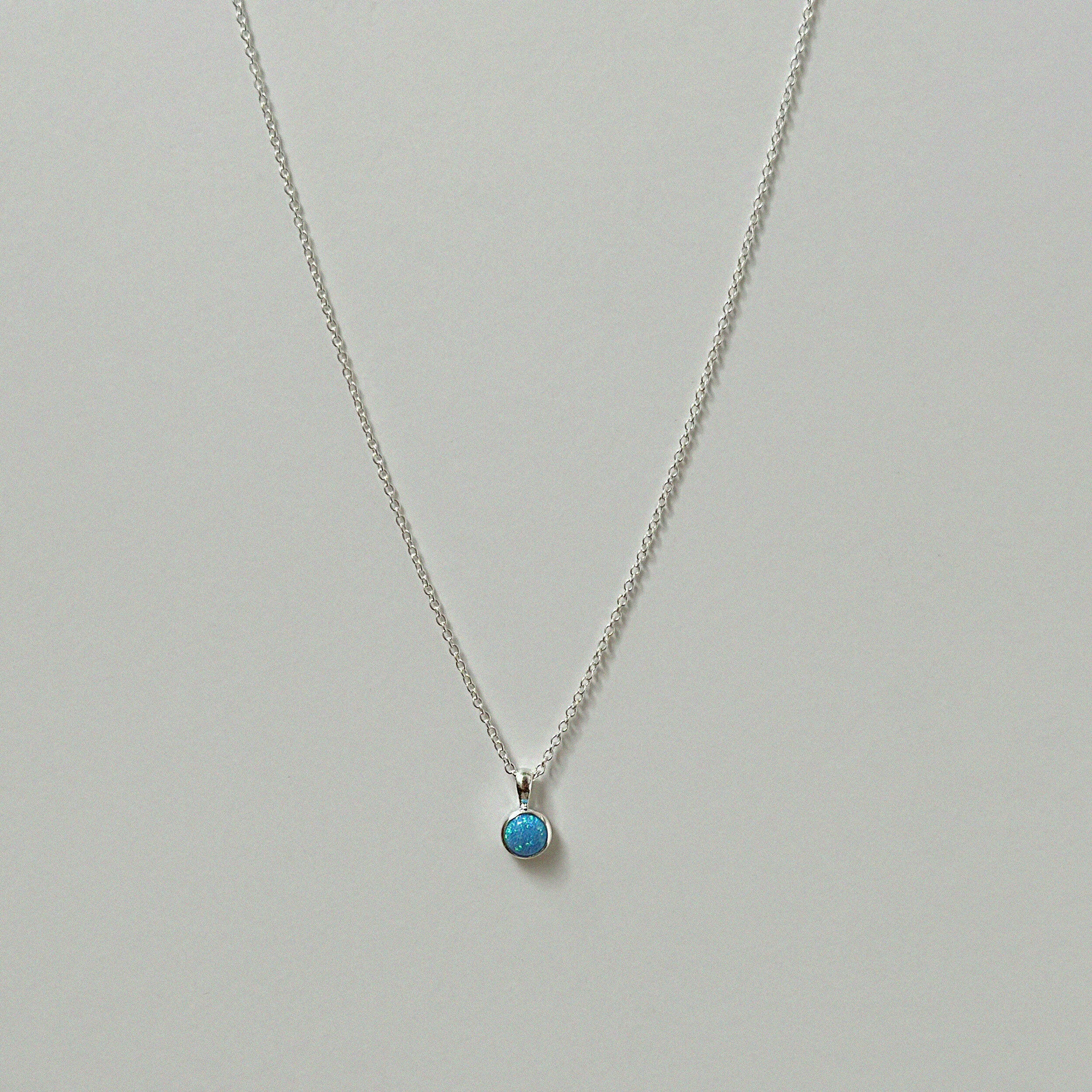 Small blue opal pendant necklace in silver laid flat on a neutral background.