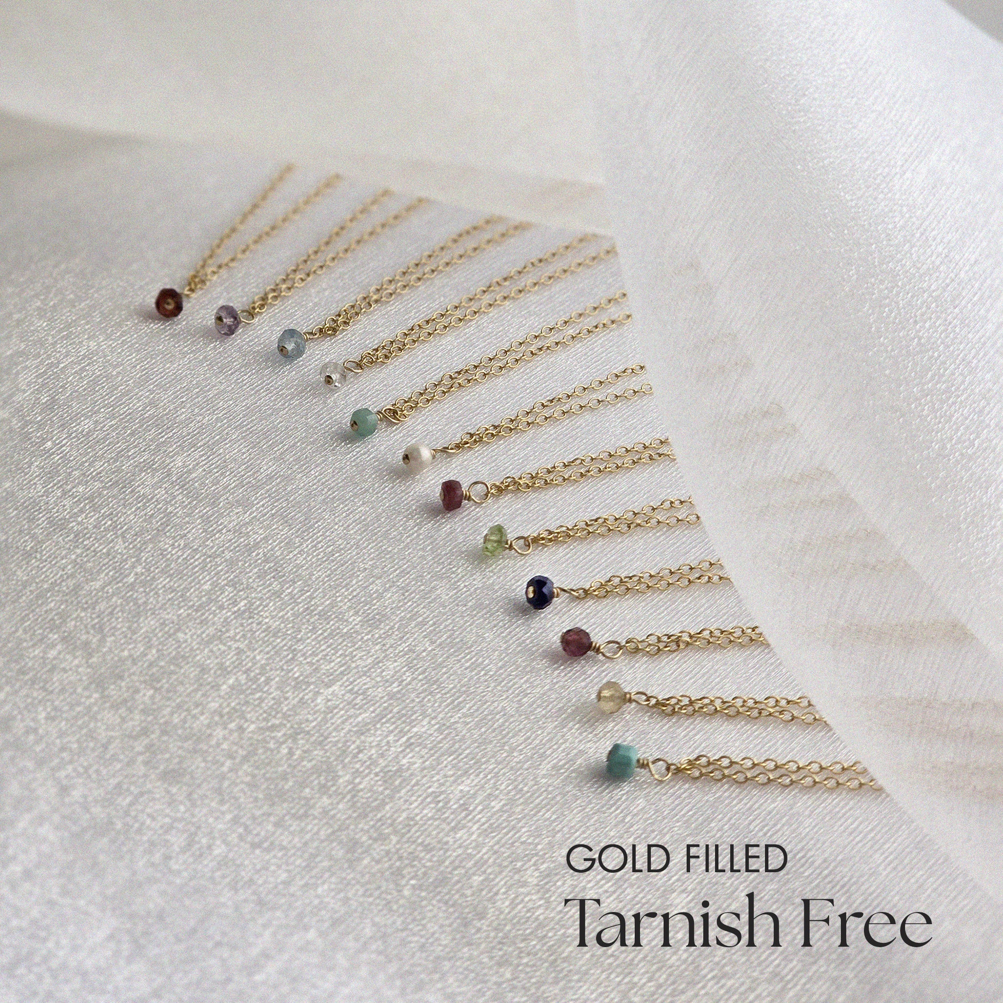 Gold filled necklaces with gemstones on a white fabric background