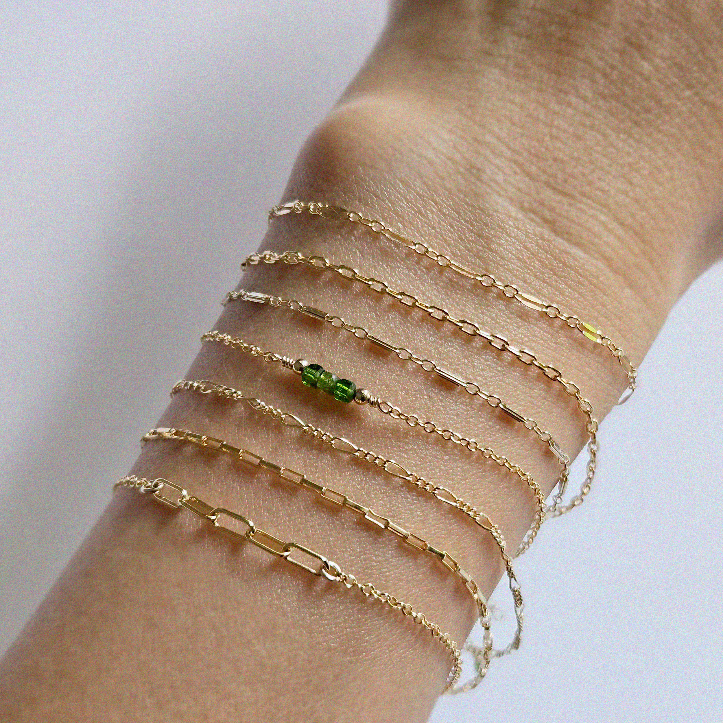 Model wearing multiple of gold filled minimal designed chain bracelets on wrist