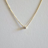 Gold necklace with a small diamond pendant on a light gray background