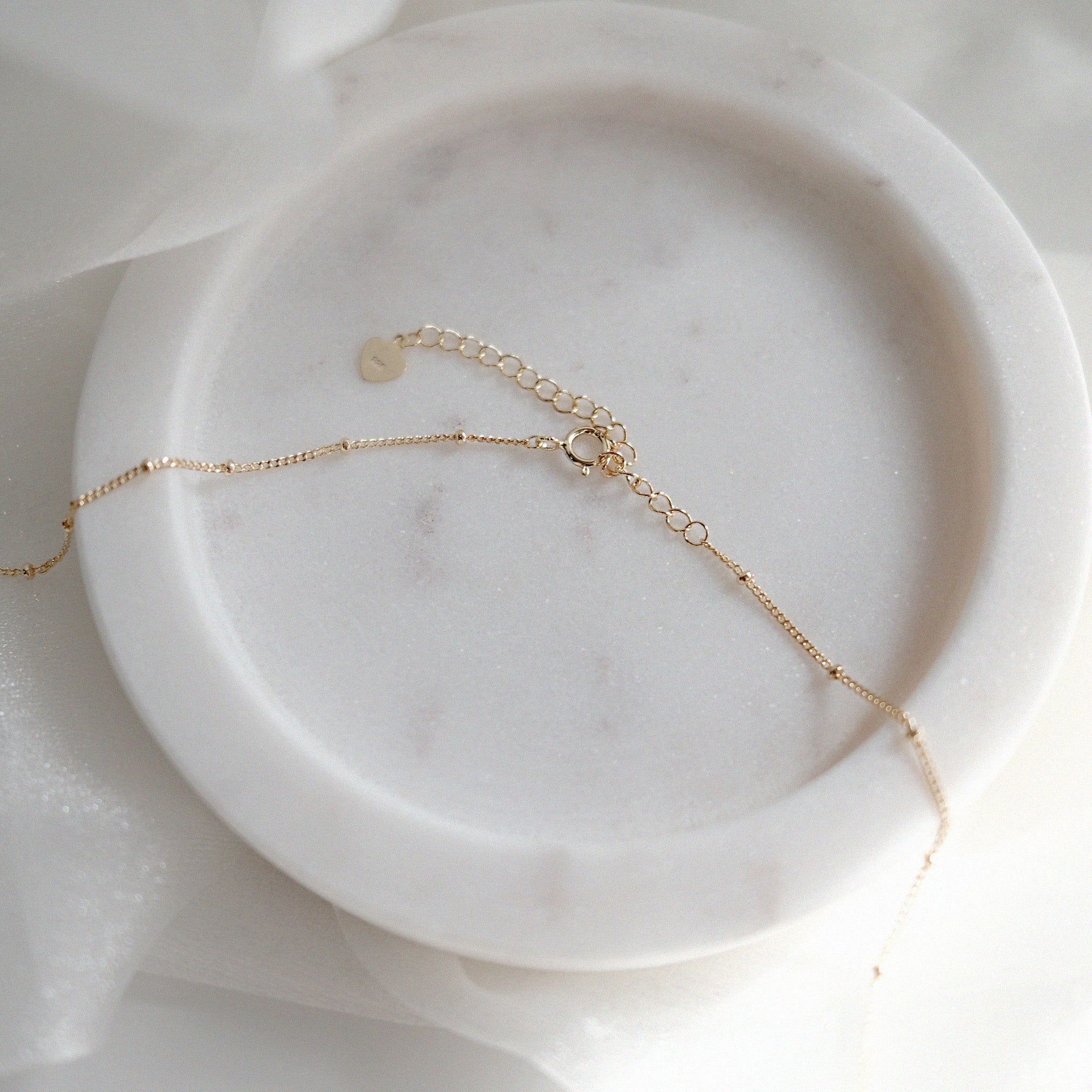Gold clasp on dainty dotted chain on a marble surface