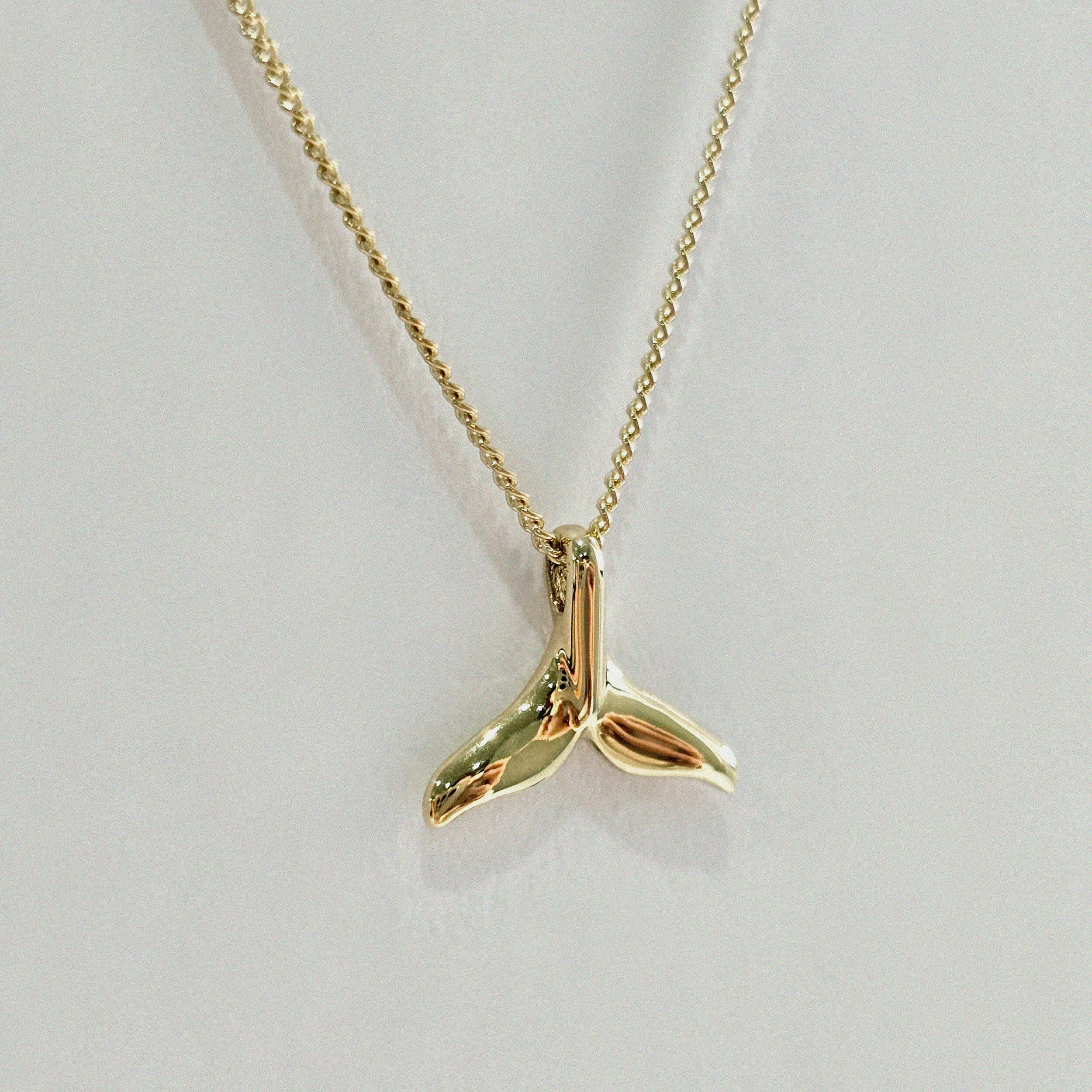 Close-up shot of whale tail pendant in 14K gold – polished surface and delicate curves