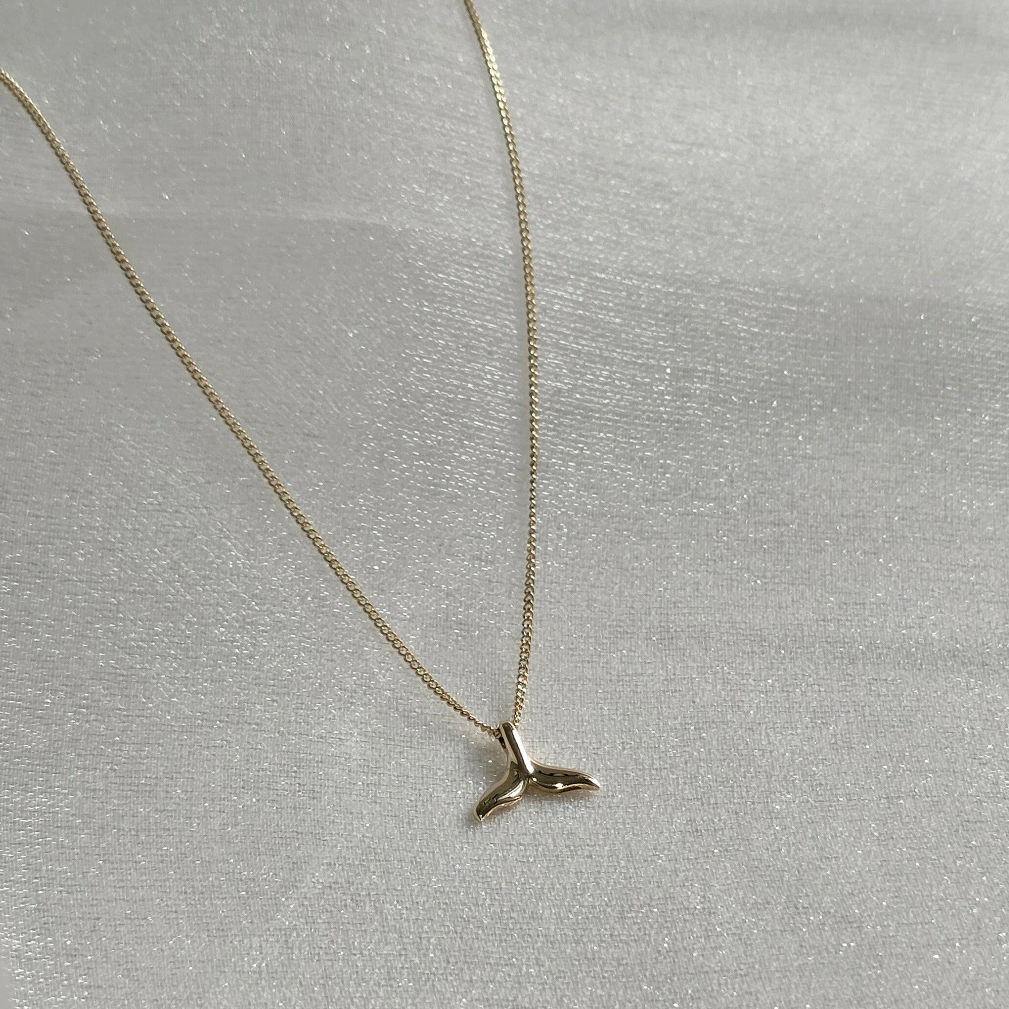 Side view of whale tail pendant showing subtle curvature and reflective finish